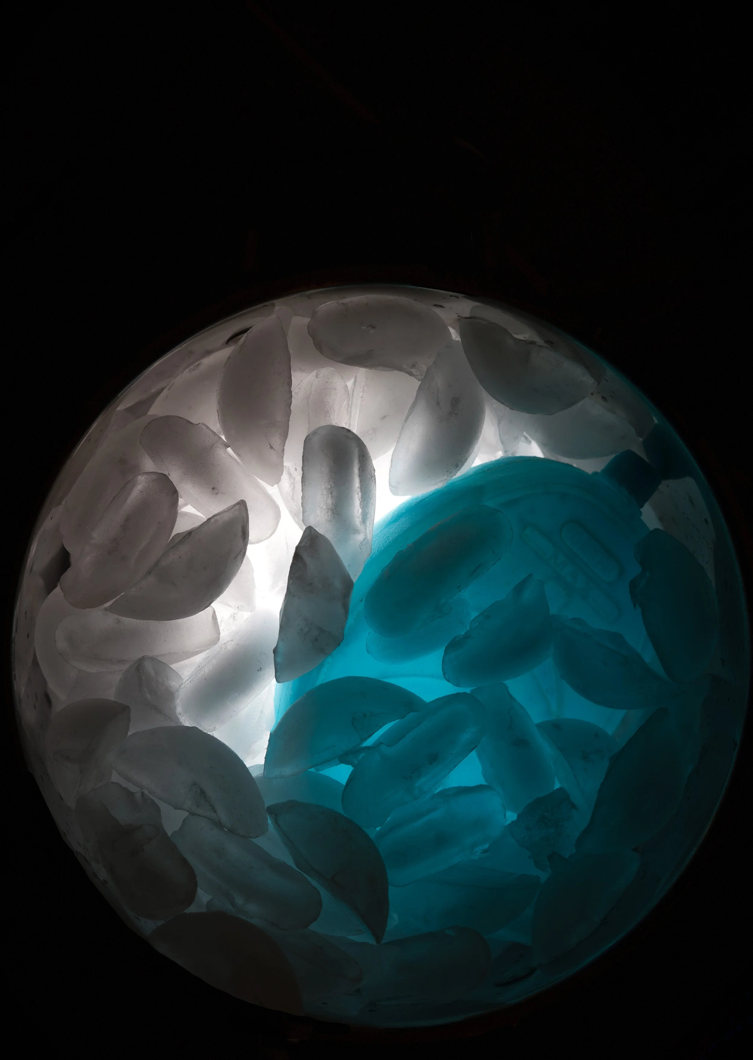 Close-up view of a bowl filled with irregularly shaped ice cubes, illuminated from below with blue and white light, creating a glowing effect.