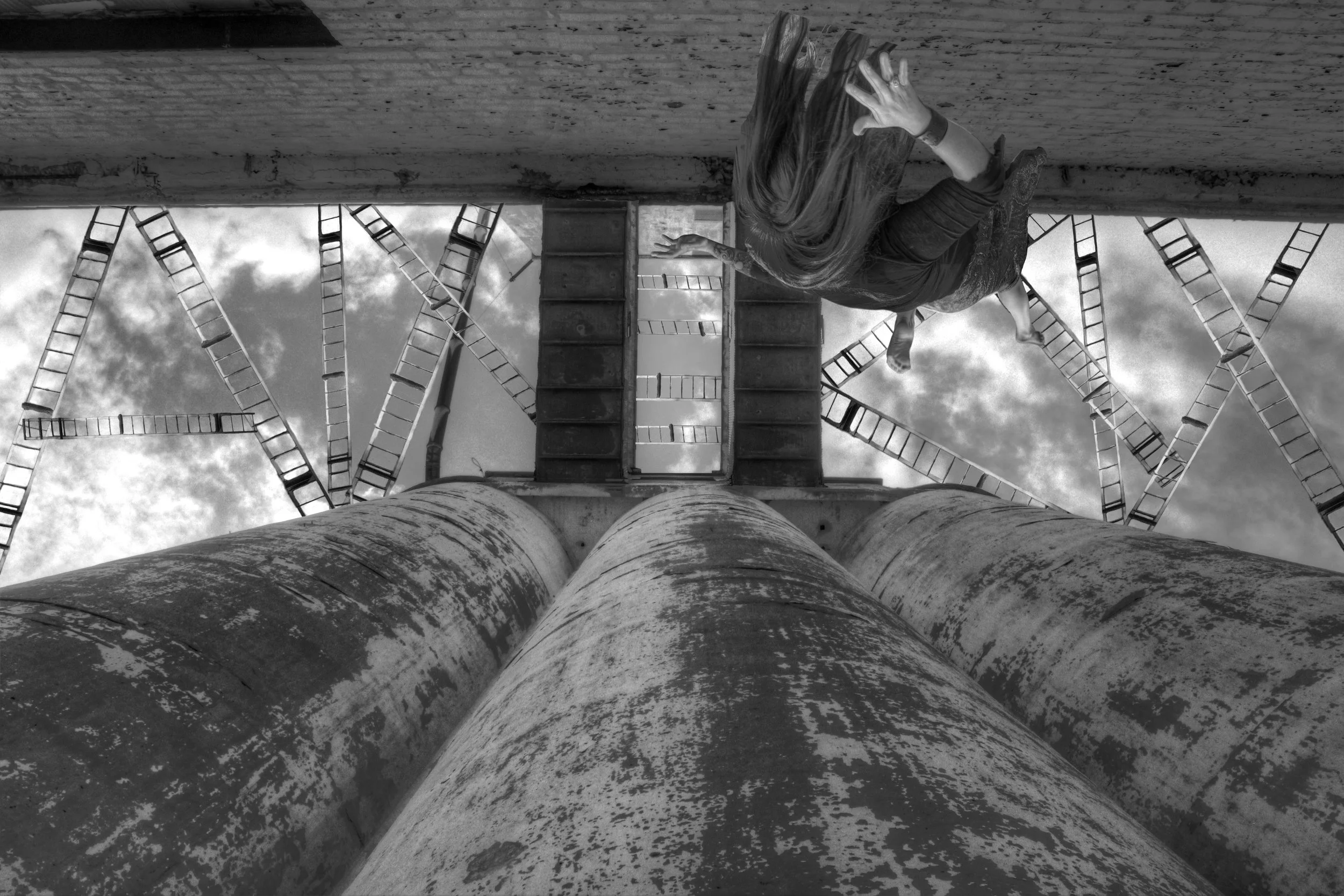 Looking up at tall weathered industrial pipes with ladders in the background and a partly cloudy sky.