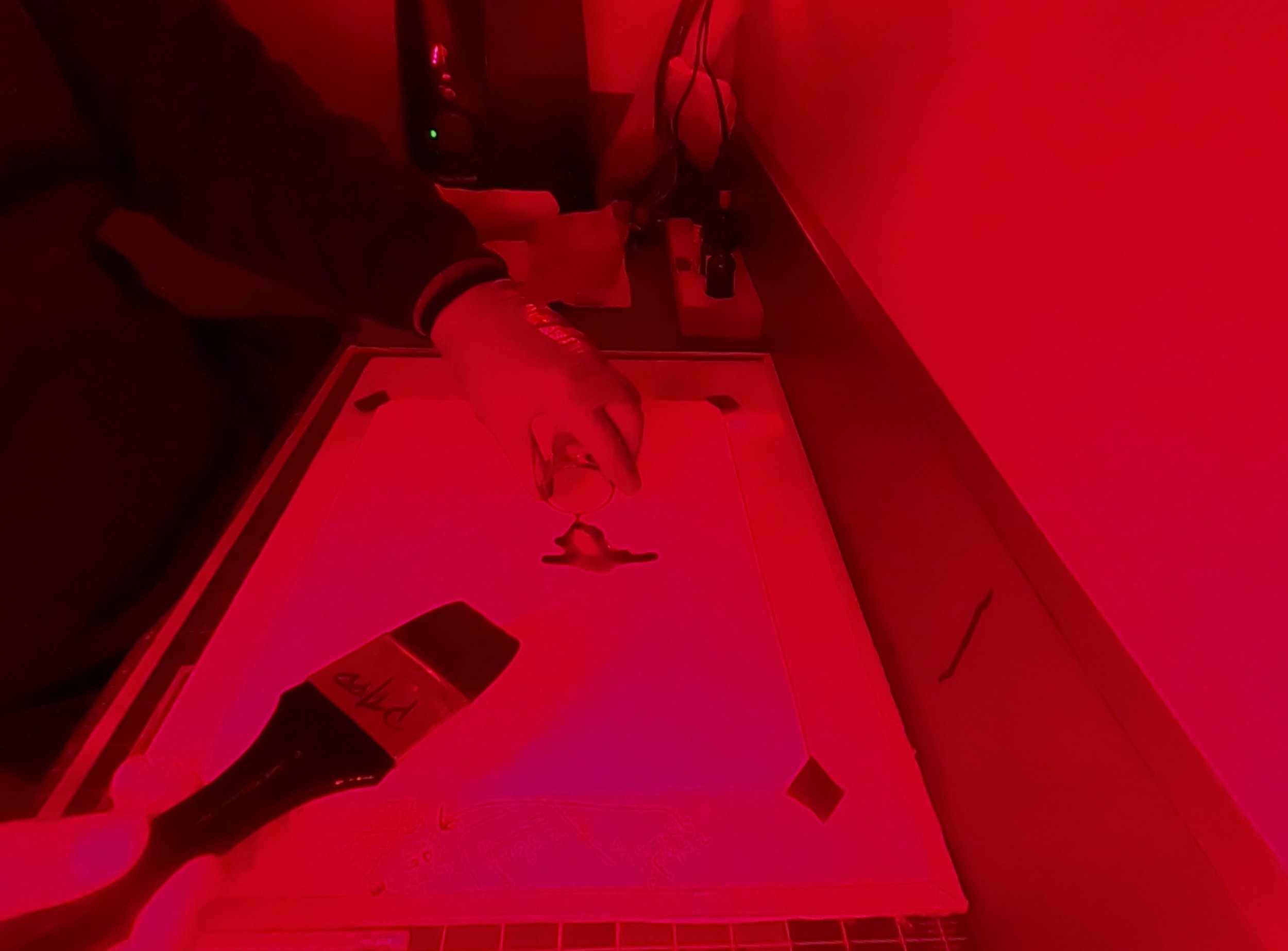 A Robin North pouring platinum palladium emulsion as he coats Washi Paper in front of a safelight in the darkroom.