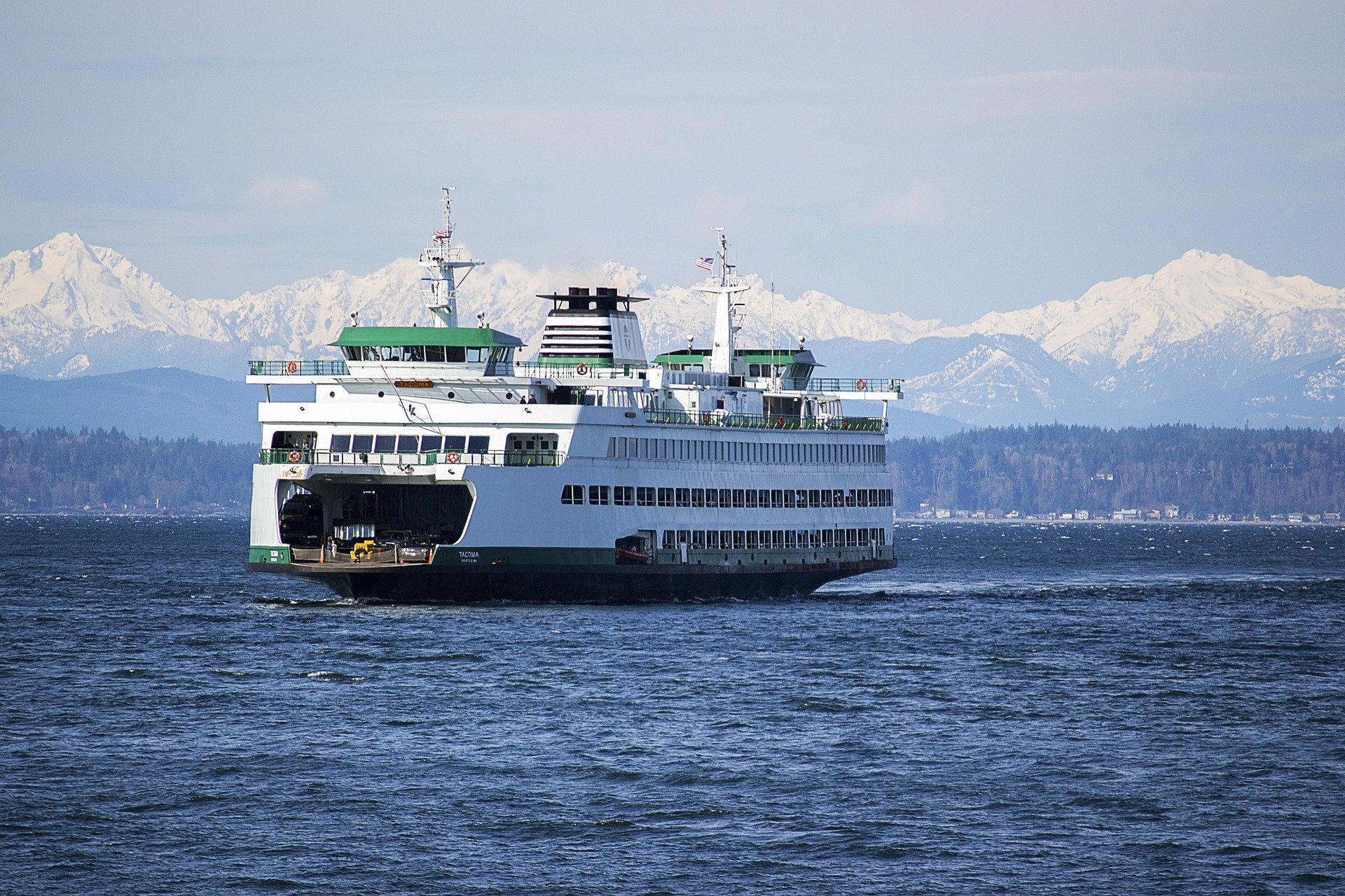 A large white ferry boat sailing on water with snow-capped mountains in the background.