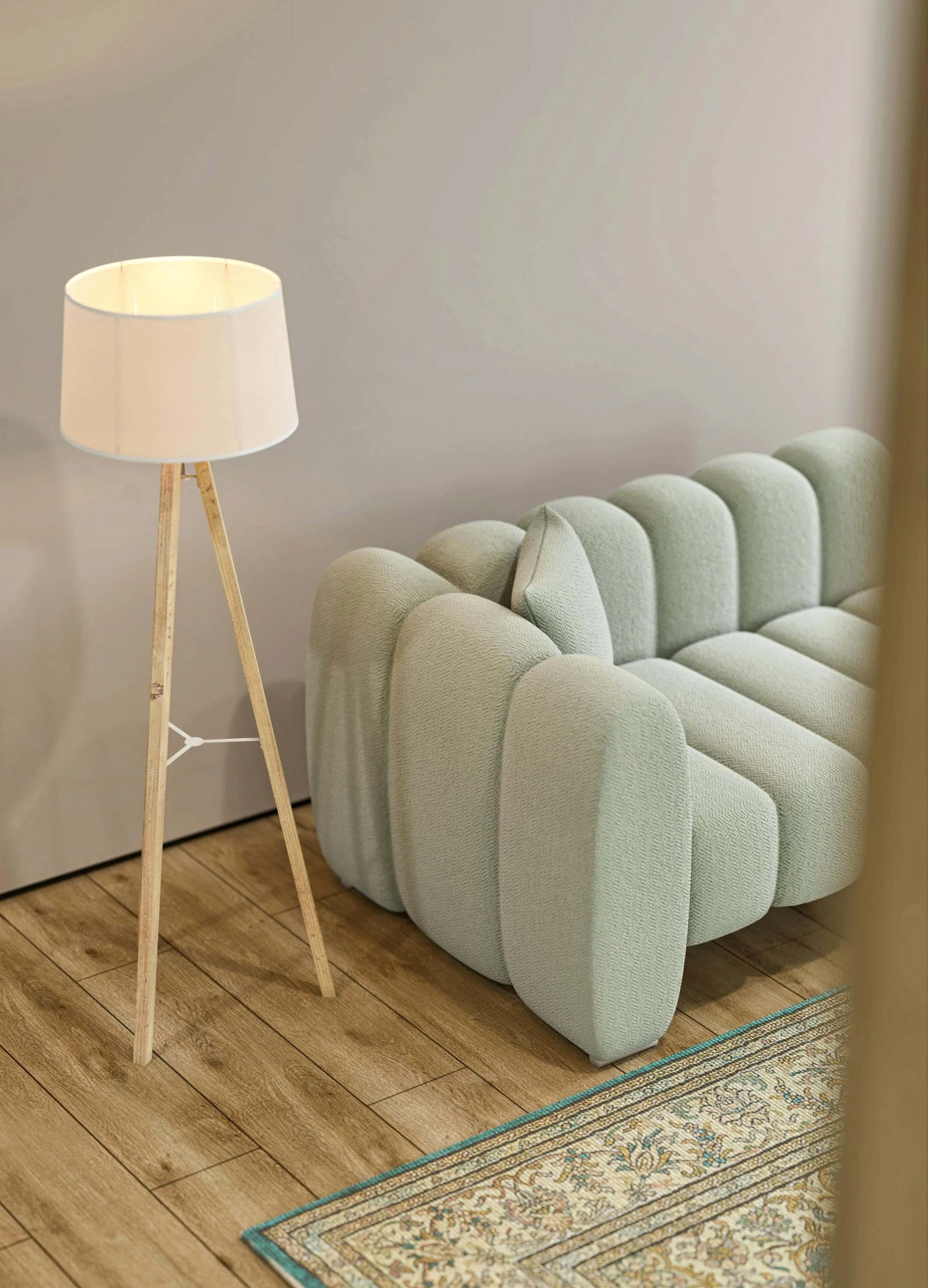 Un lampadaire en bois clair à trois pieds, avec une lampe blanche, placé à côté d'un canapé vert pâle en tissu, avec une pochette de coussin assortie, sur un sol en bois clair avec un tapis à motifs.