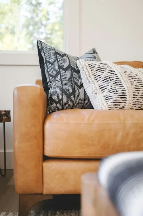 Canapé en cuir beige avec deux coussins, un noir et blanc avec un motif géométrique, et un autre coussin crème avec des rayures