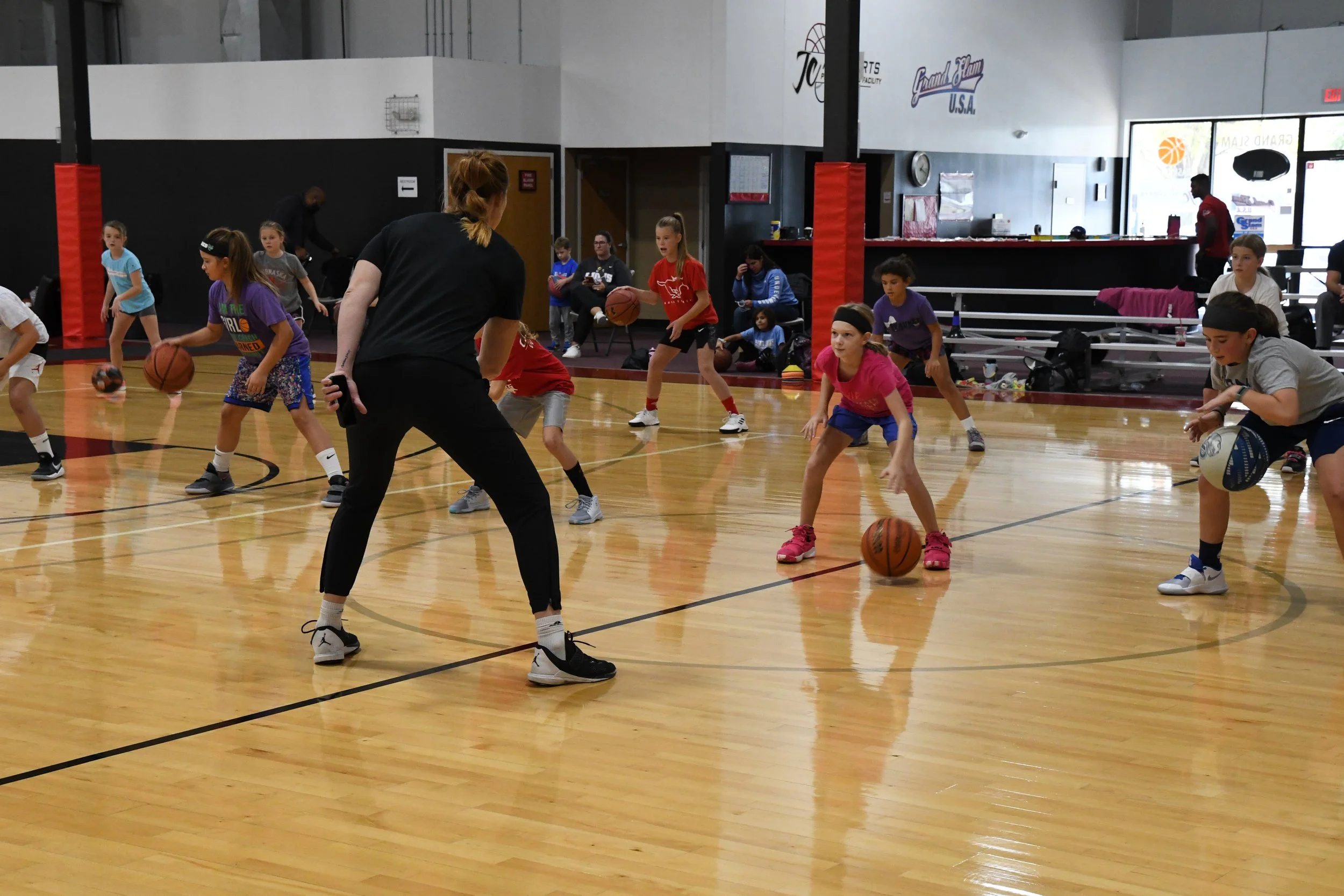 Young girls practicing basketball drills in an indoor gym, with a coach overseeing their practice.