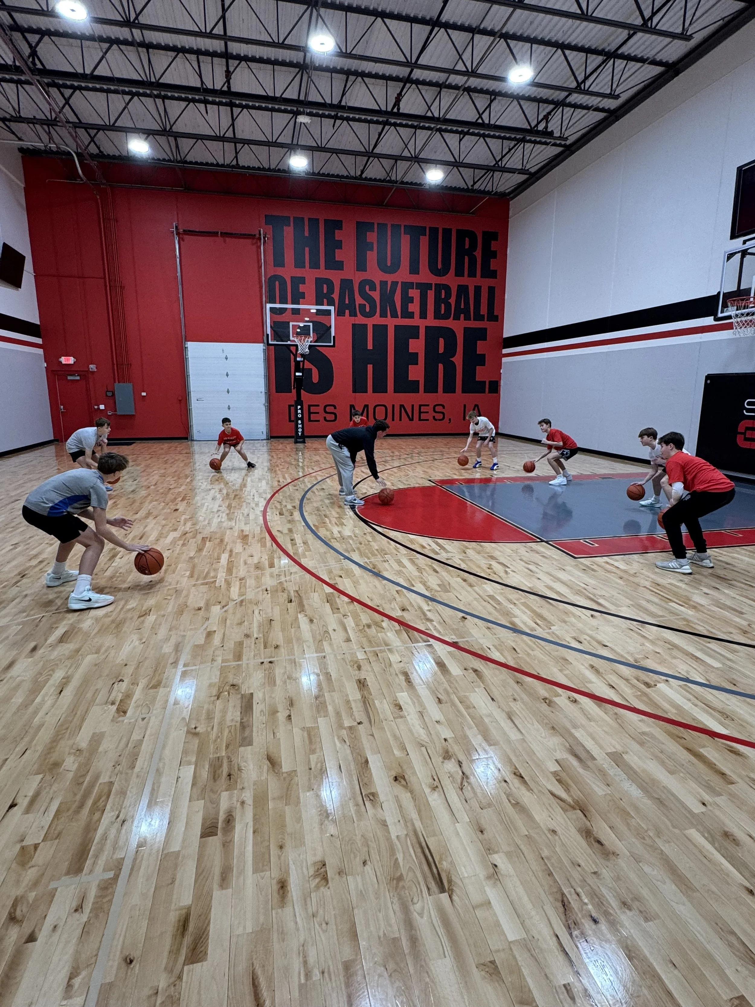 Young basketball players practicing dribbling drills on an indoor basketball court with a large sign reading "The future of basketball is here" in the background.