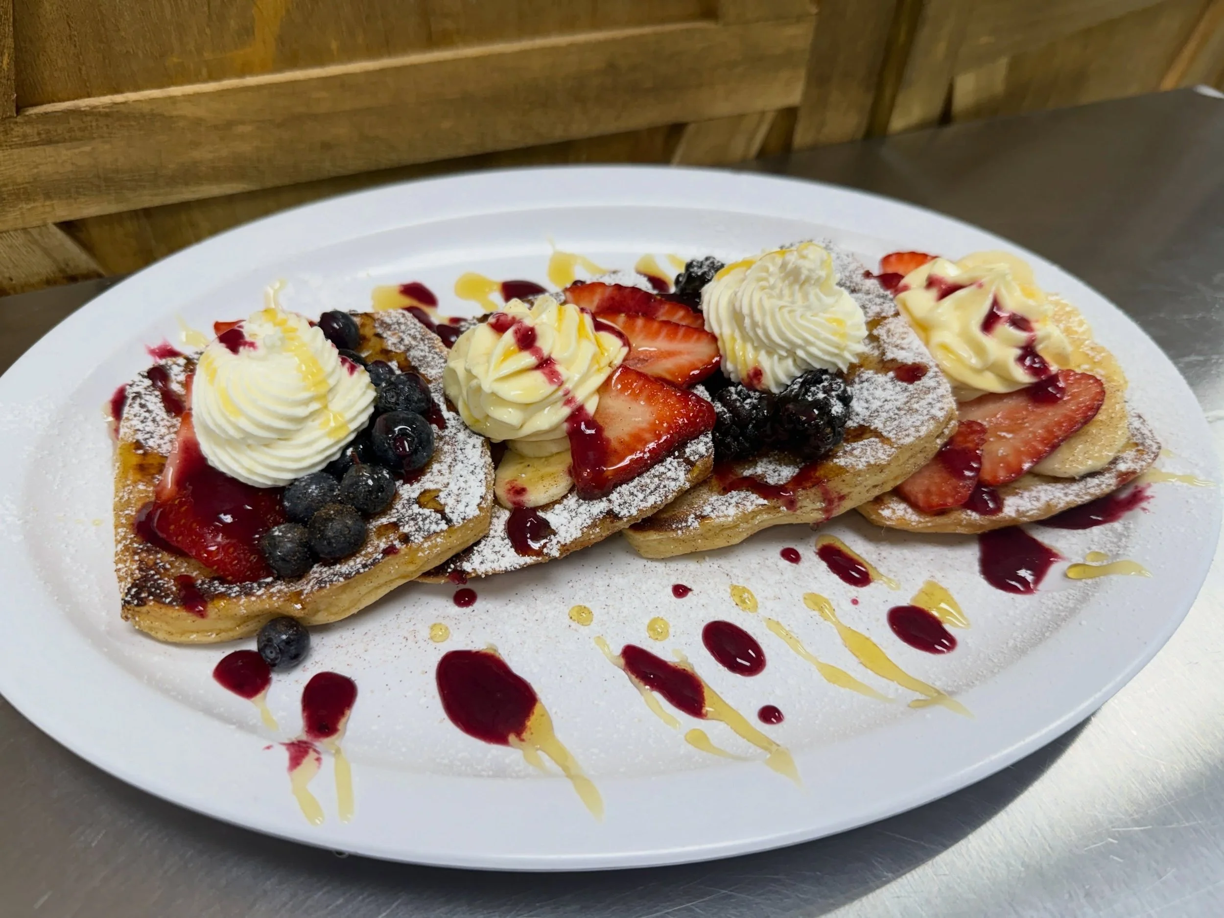 Plate of waffles topped with whipped cream, strawberries, blueberries, and drizzled with red and yellow syrup, dusted with powdered sugar.