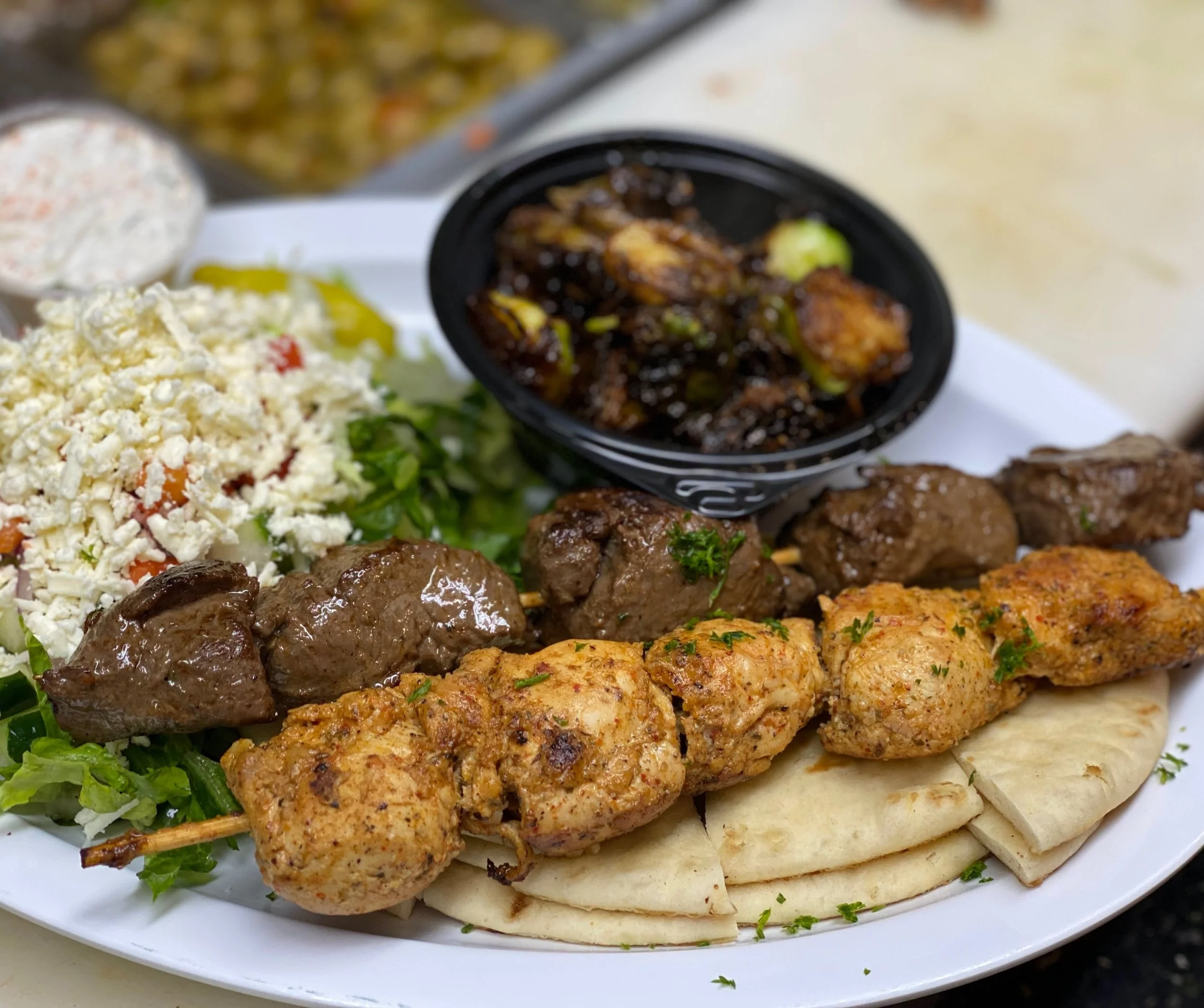 Close-up of a plate of Middle Eastern kebabs, including grilled meat skewers, fresh salad, and flatbread, with a side of sauce.