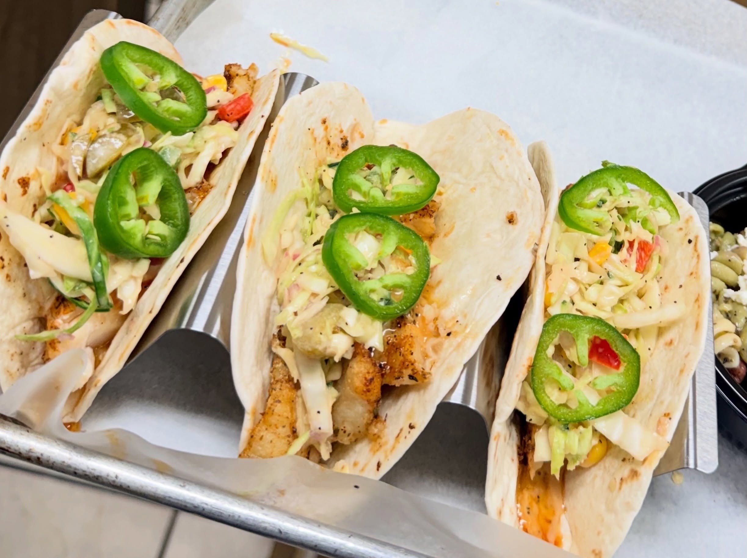 Multiple tacos with various fillings including sliced green peppers, shredded lettuce, vegetables, and sauces on a tray.