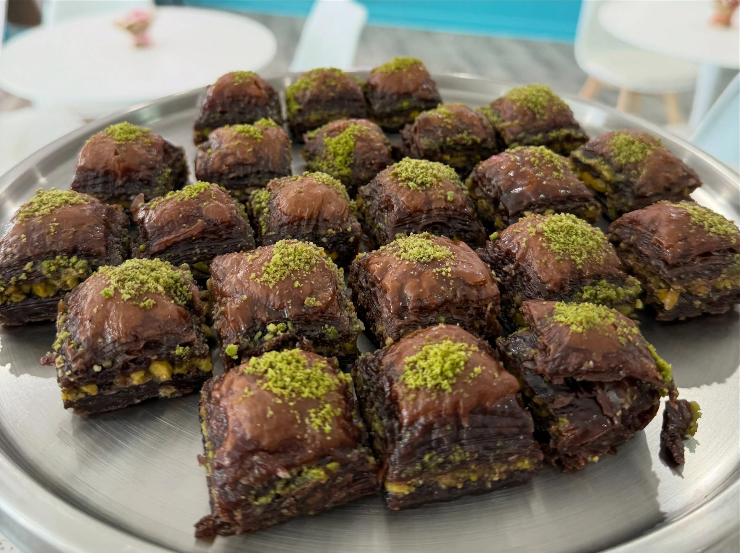 A tray of chocolate-covered desserts topped with green pistachio crumbs, arranged in rows.