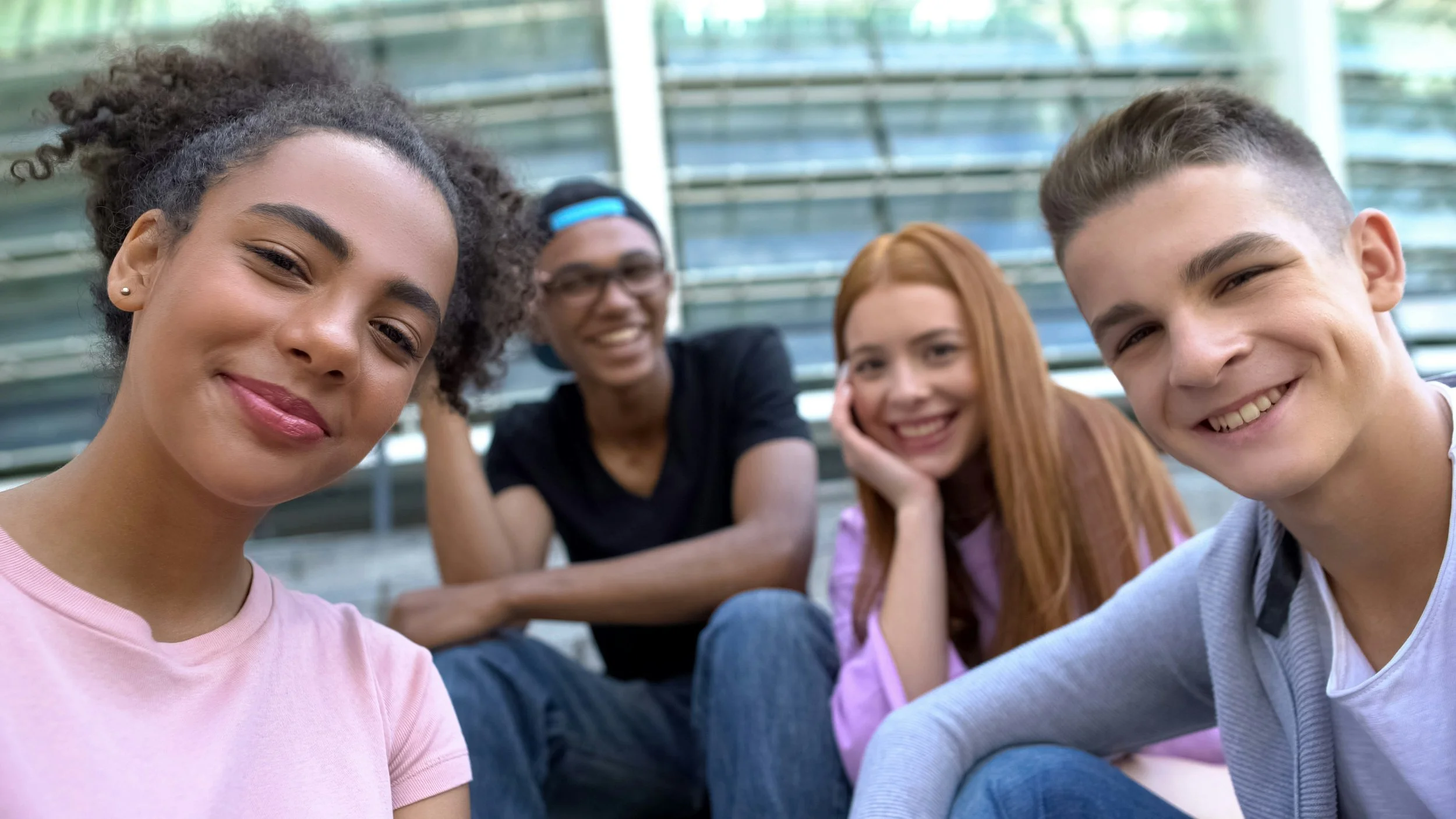 Four young adults sitting on outdoor bleachers taking a selfie, smiling, with two women and two men.