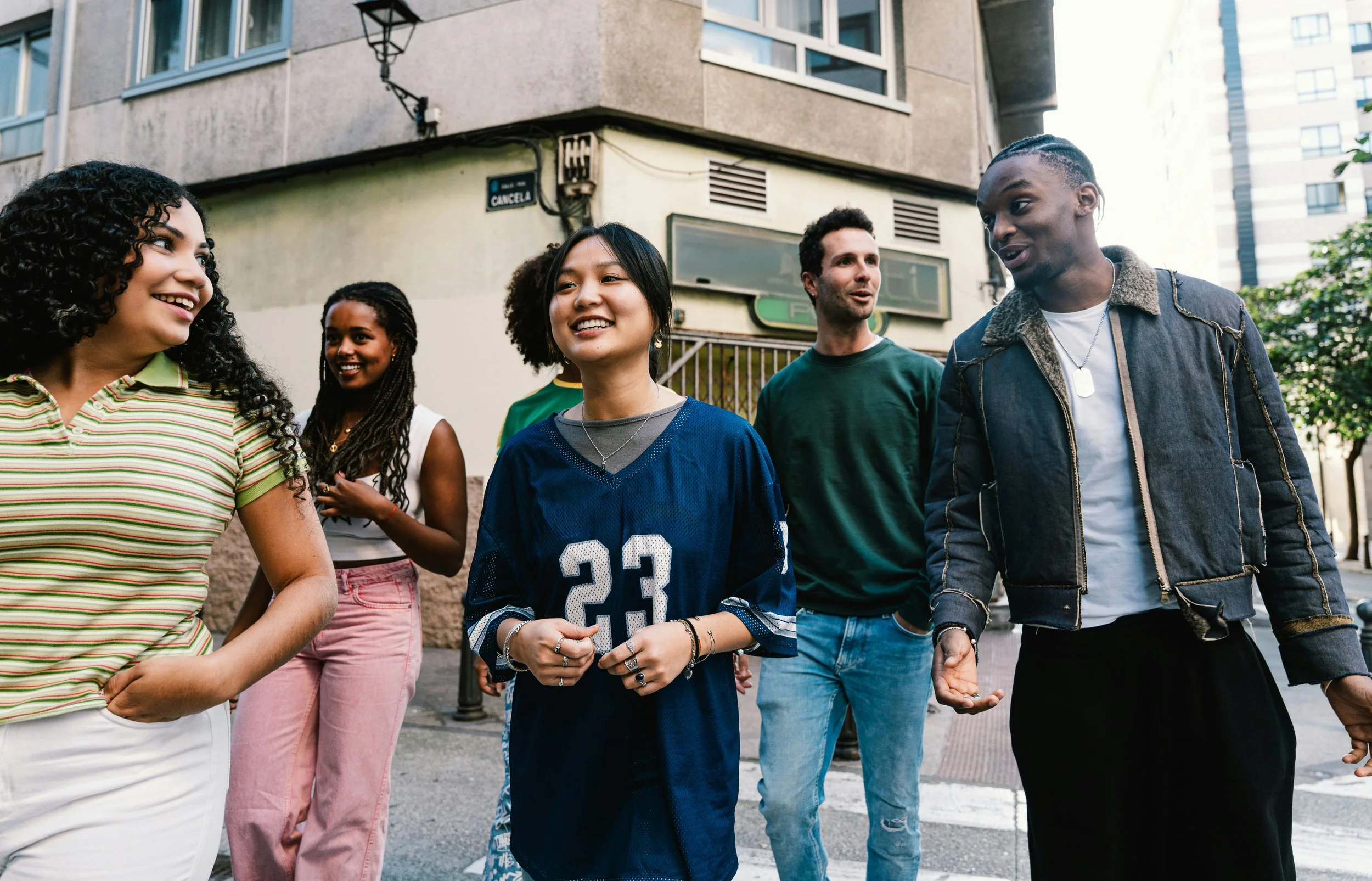 Group of five diverse friends walking together on city street, smiling and talking.