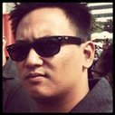 A young man with short black hair wearing sunglasses and a dark jacket, outdoors.