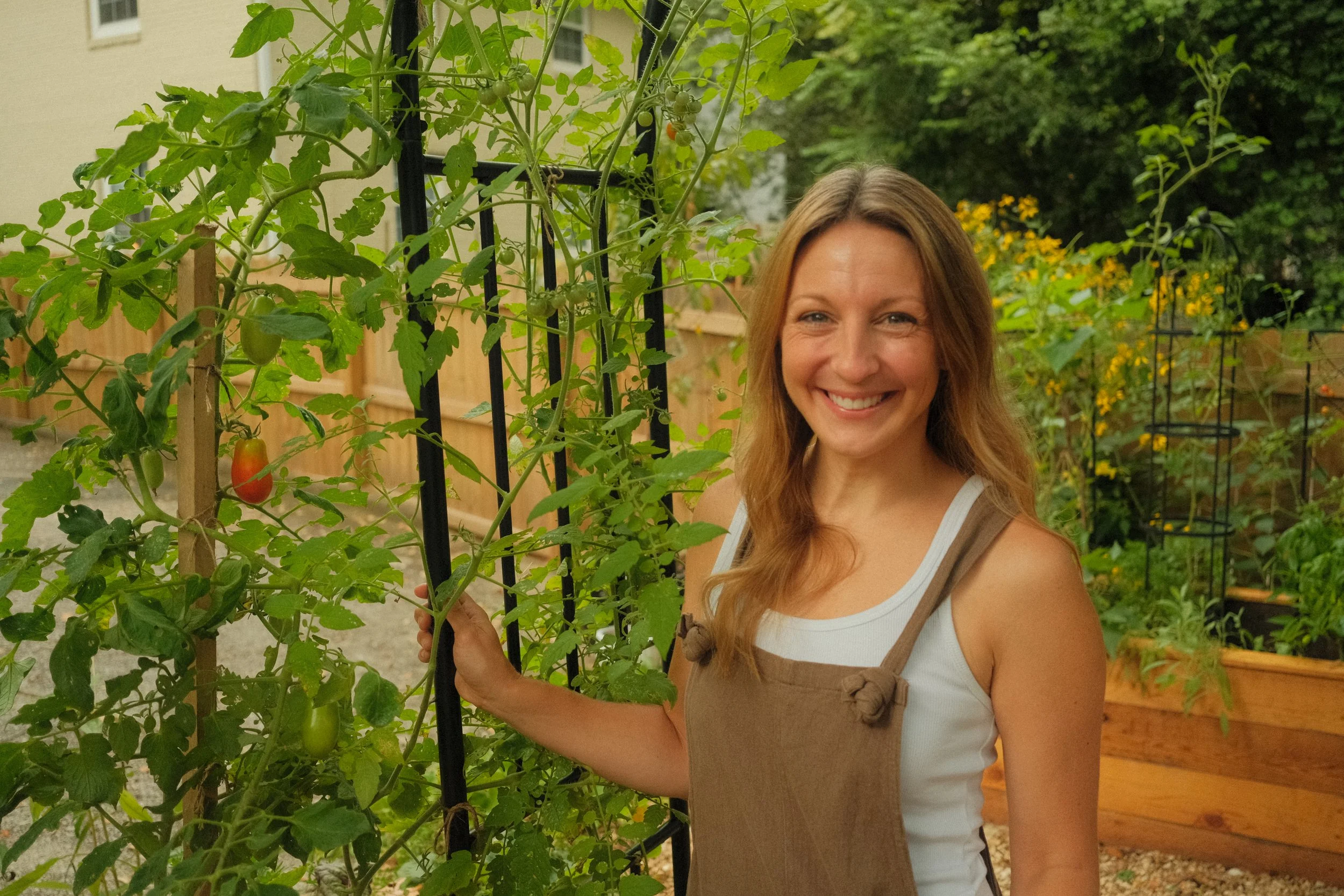 Owner and Founder of Marigold Gardening, LLC standing in her kitchen garden under an arched trellis covered with cherry tomatoes.