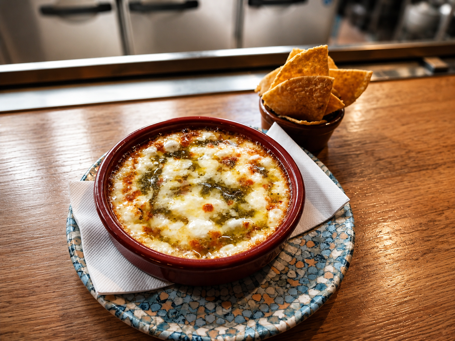 Baked Provolone cheese dip with herbs and jalapeno glaze in a red bowl, served with tortilla chips on a small plate on a wooden table.