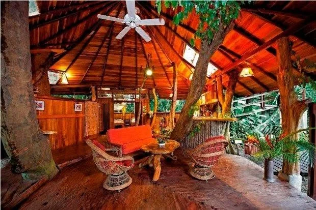 A tranquil treehouse room in Bali with a thatched roof, ceiling fan, and comfortable wicker furniture offers a warm and inviting space for a journaling workshop.
