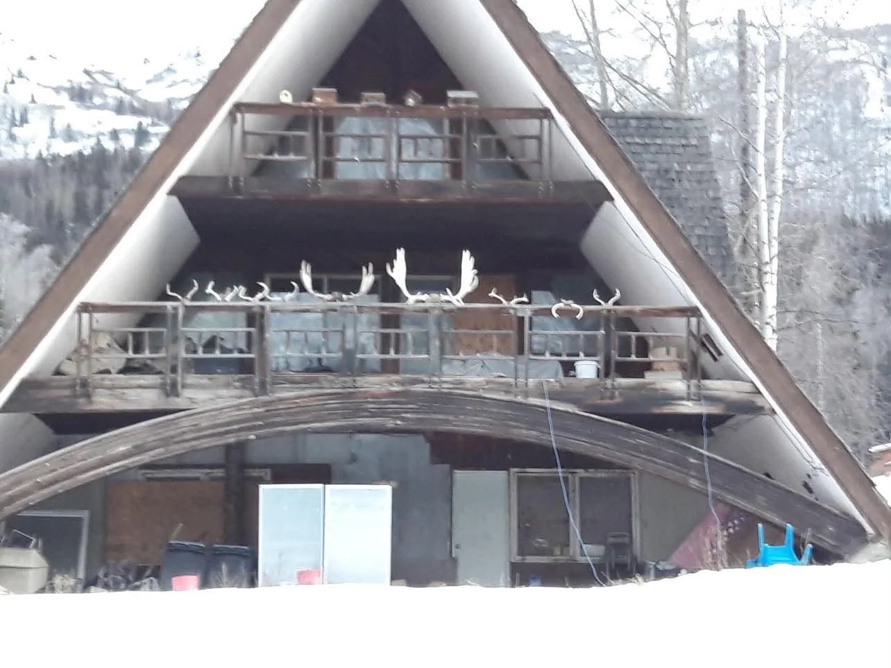 A rustic A-framed cabin sits in a snowy mountain landscape.