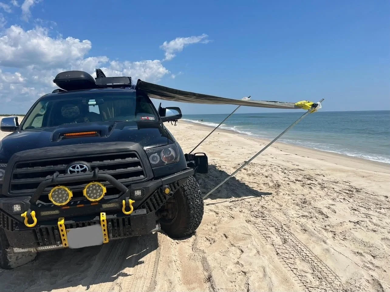 Al's customized, rugged black Toyota Sequoia truck basks in the sun on the beach at Assateaque Island. The canopy is open, casting an inviting shadow on the sand.