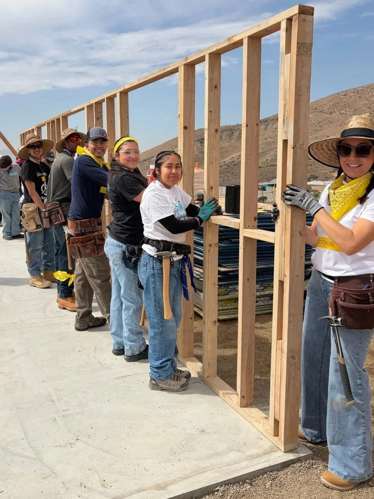 Group of volunteers working together to build a wooden frame for a structure outdoors, in a desert or arid landscape.
