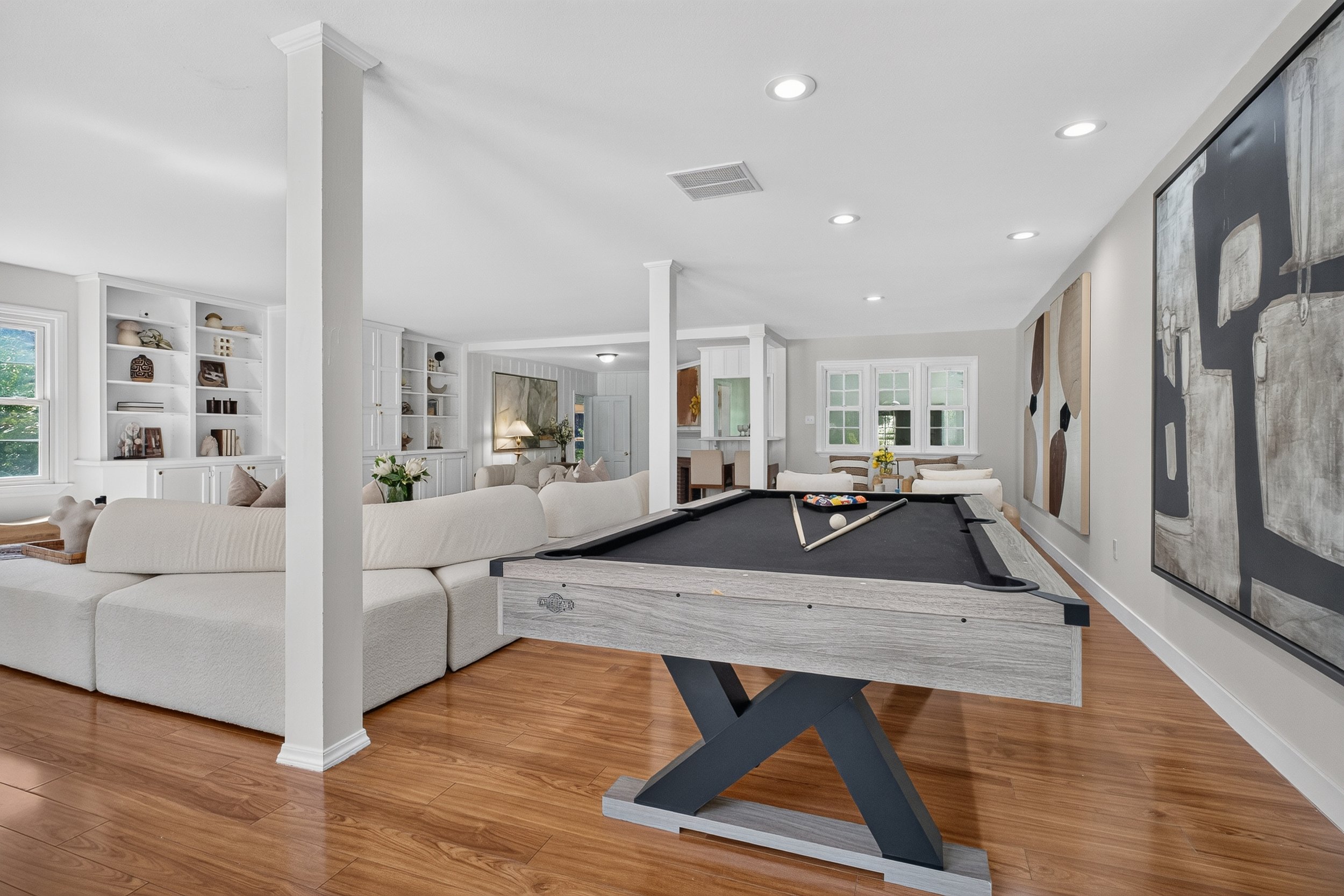 Living room with white couch, pool table, built-in white bookshelves, and large windows in the background.