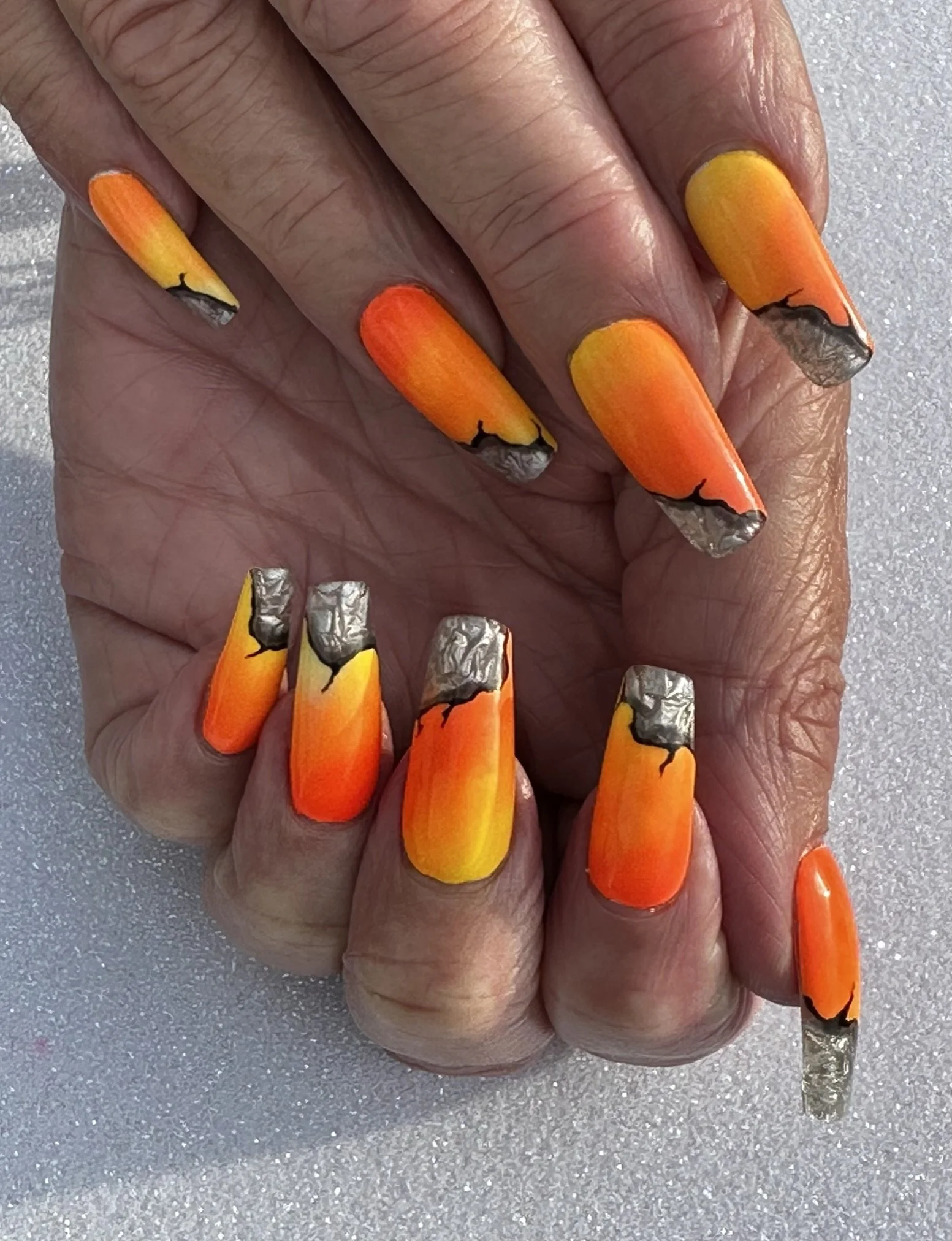“Bright orange and yellow gradient nail art with black and silver details, created by Roses Kustom Worx in Taupō.”