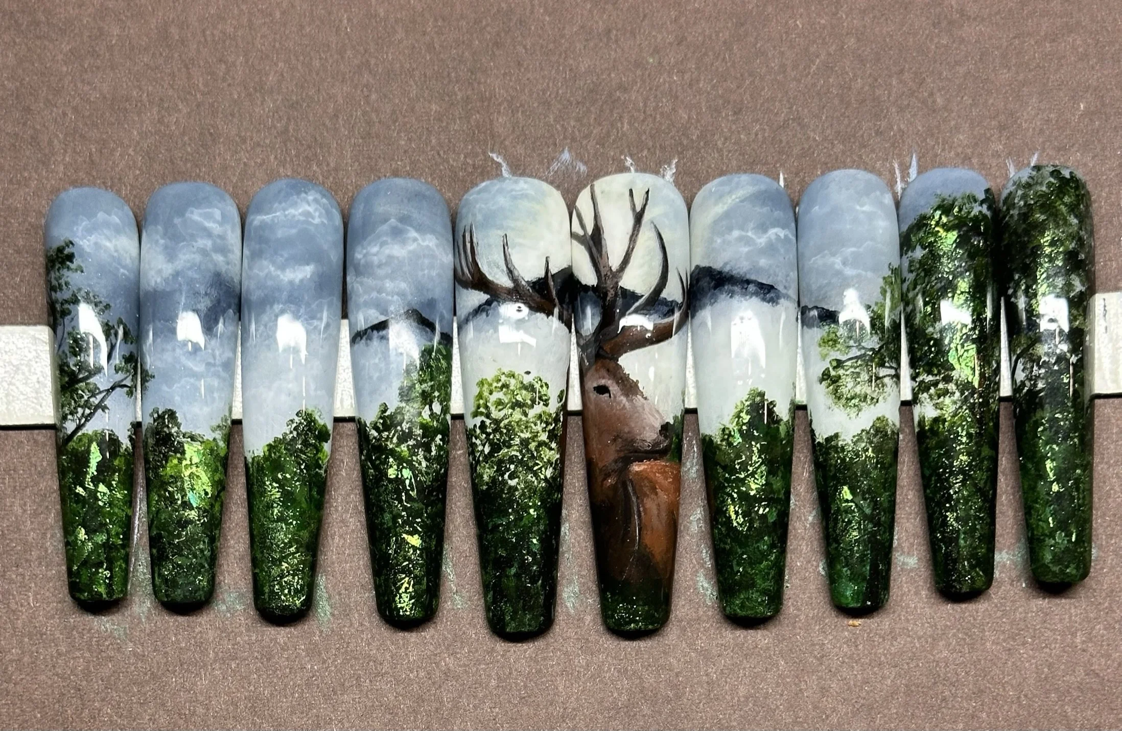 “Hand-painted nature-inspired bespoke nail art featuring a stag, forest and mountain landscape by Roses Kustom Worx in Taupō.”