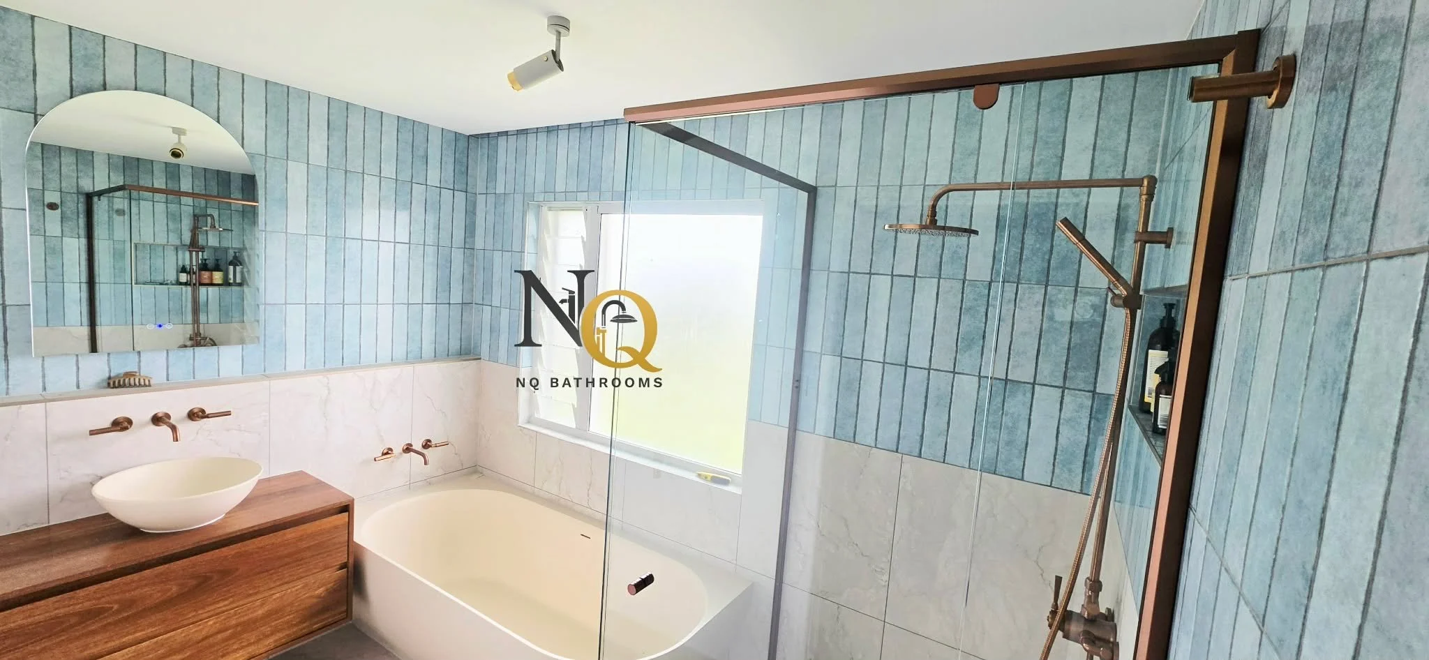 Modern bathroom with blue vertical tile walls, a bathtub, a vessel sink on a wooden vanity, a large mirror, a frosted window, and a walk-in shower with a copper showerhead and fixtures.