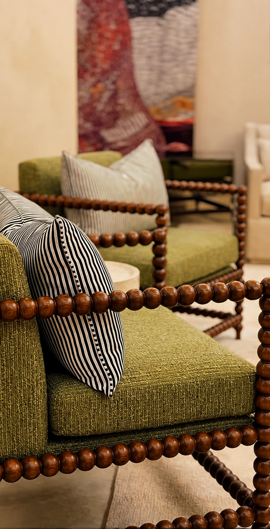 Close-up of a green vintage armchair with a black and white striped pillow, wooden bead armrests, and stacked pillows behind it, in a cozy interior setting.