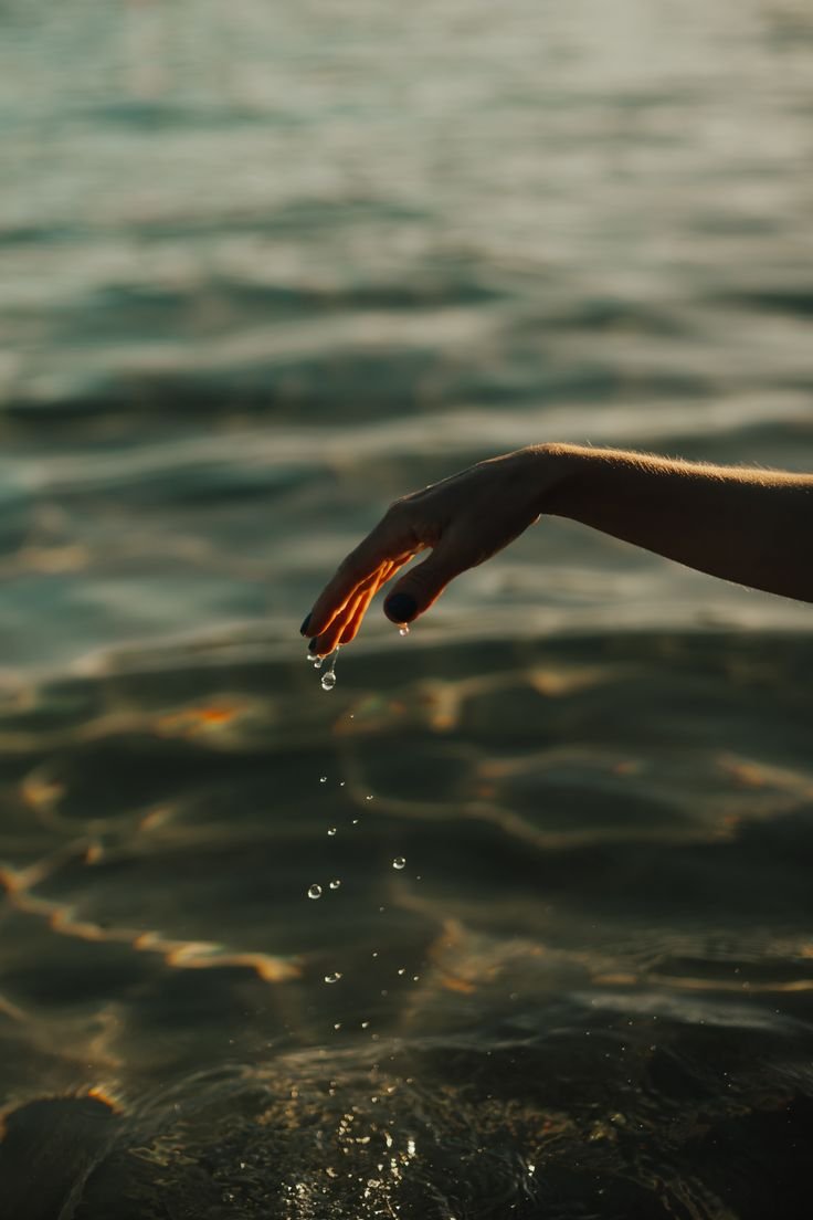 GALILEA and Beyond Consulting. Close-up of a person's hand gently dipping into water, creating small ripples and droplets.