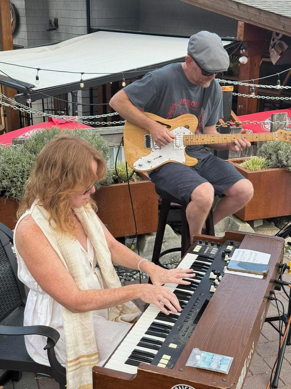 A woman playing a keyboard and a man playing an electric guitar outdoors.