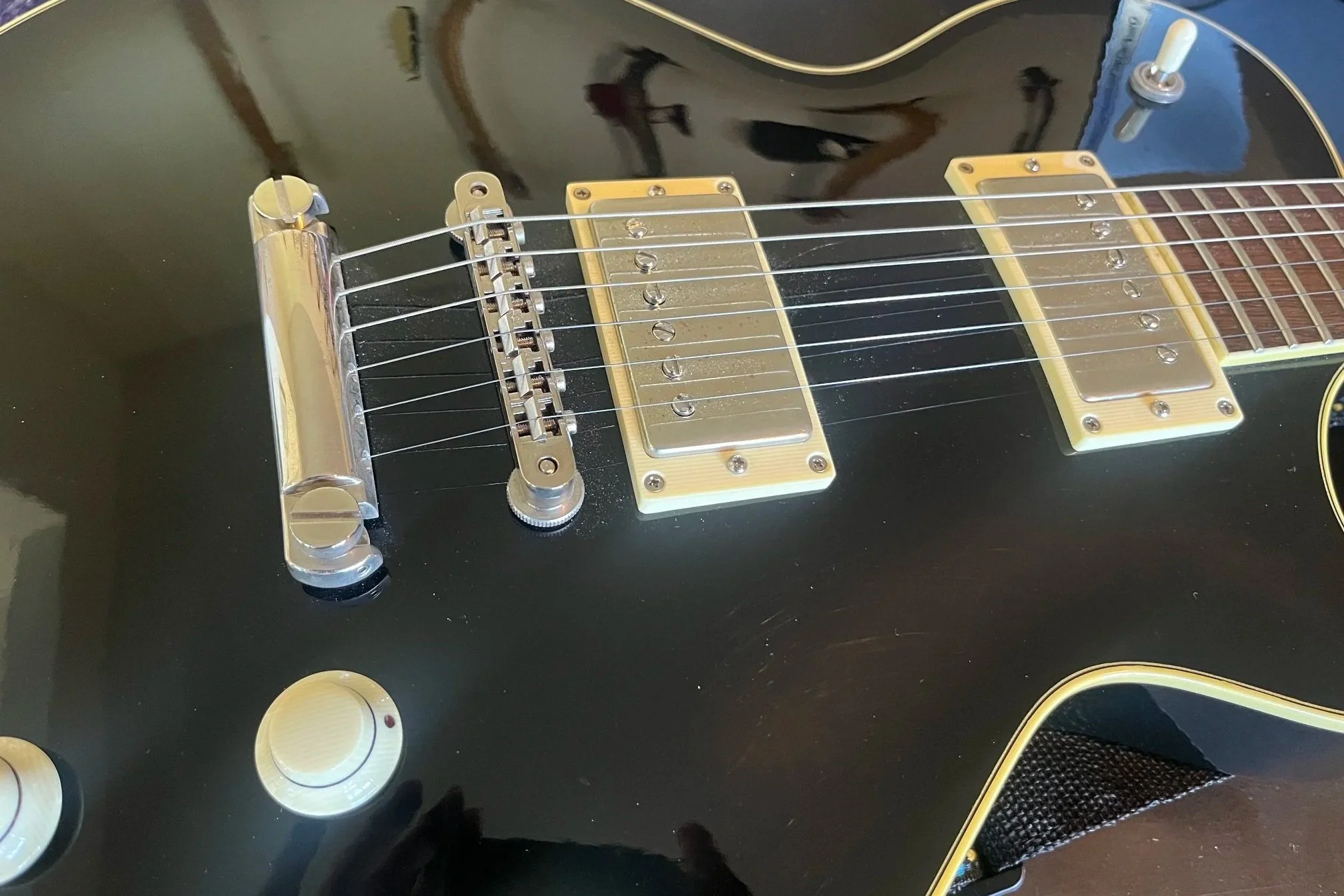Close-up of an electric guitar with a black body, yellow pickups, and gold hardware, including the bridge and control knobs, on a dark surface.