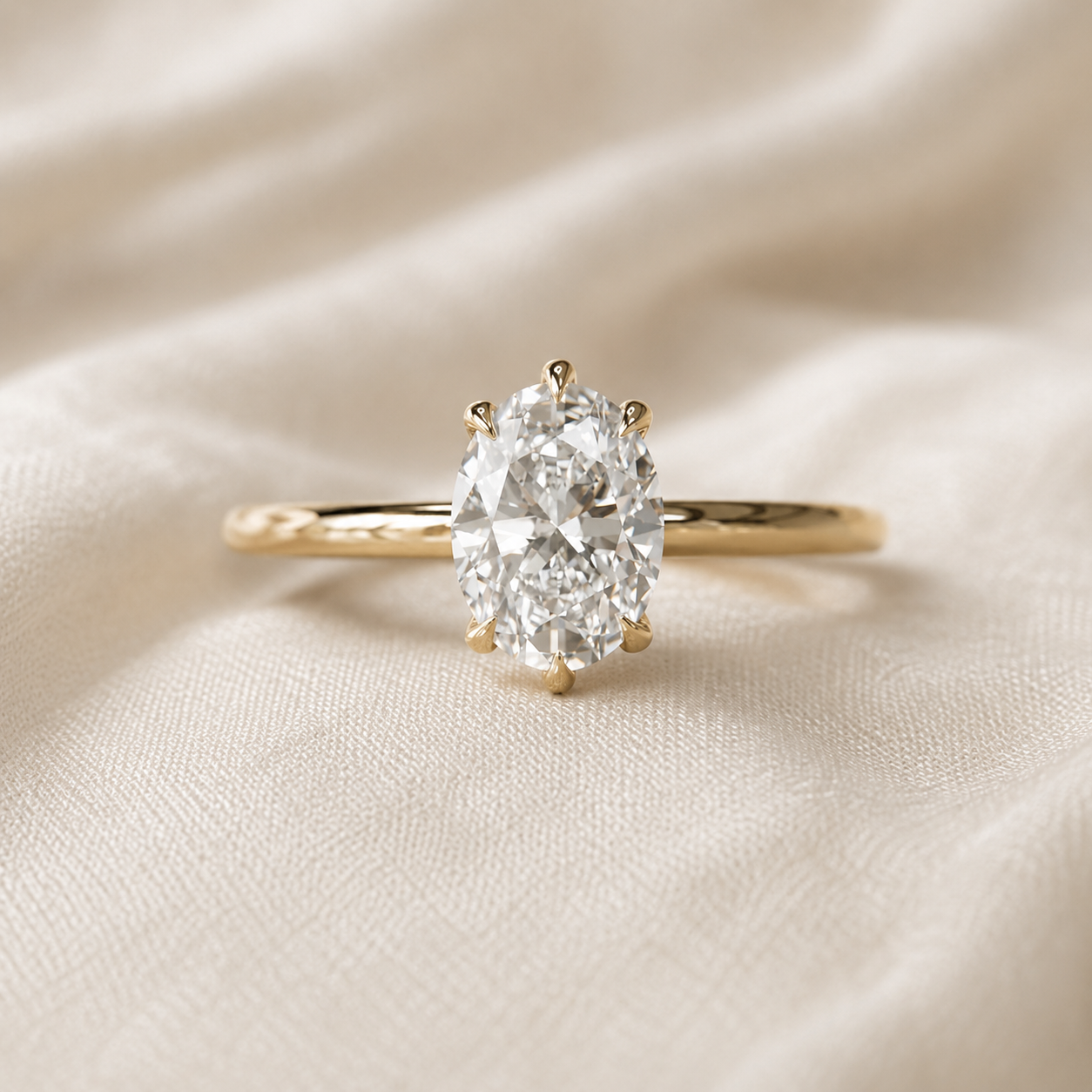Yellow Gold ring with an oval diamond solitaire setting on cream-colored satin fabric.