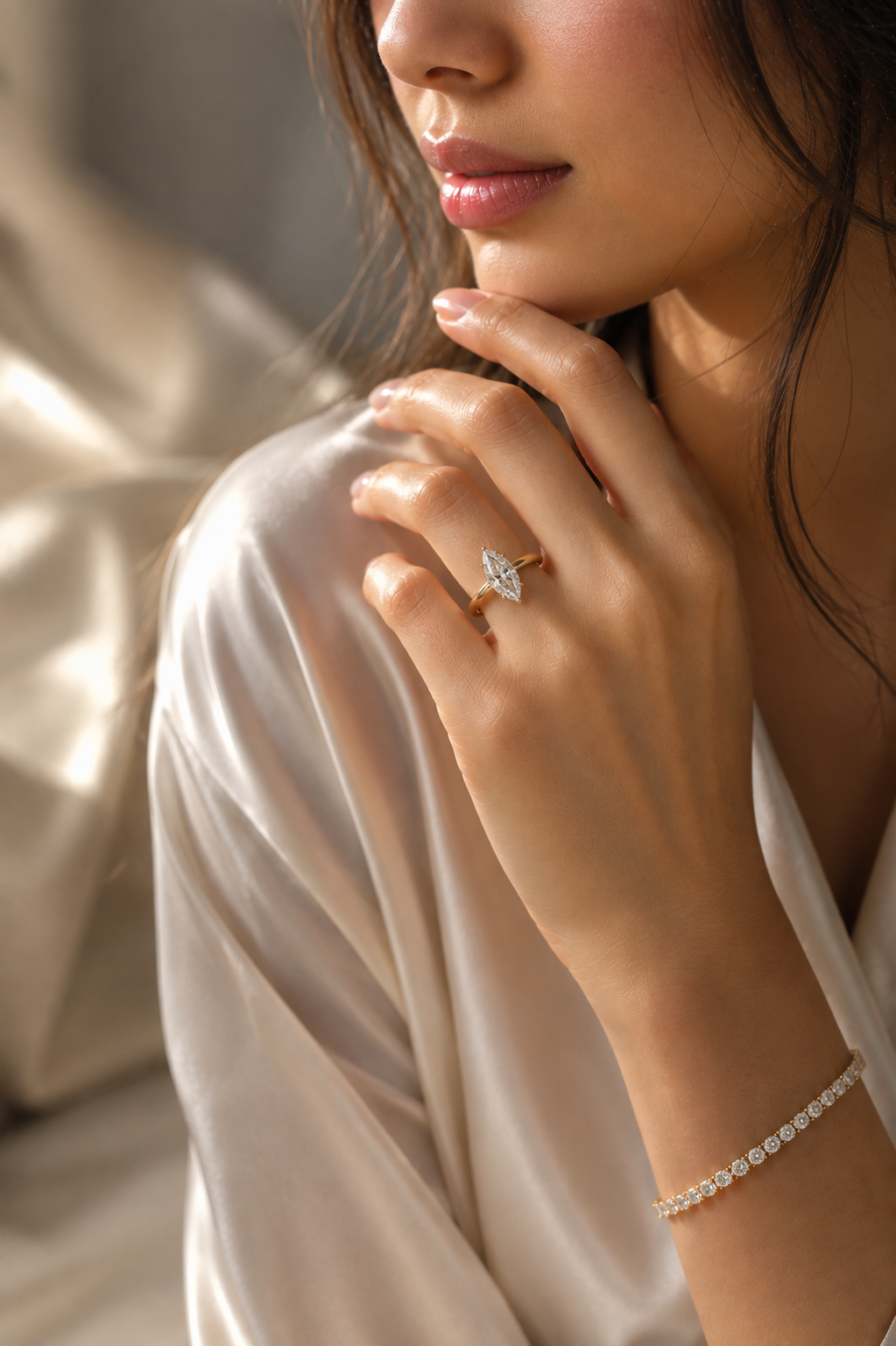 Close-up of a woman with long dark hair wearing a satin blouse, showing her left hand with a large marquise-shaped diamond engagement ring, a diamond bracelet on her wrist, and her face partially visible.