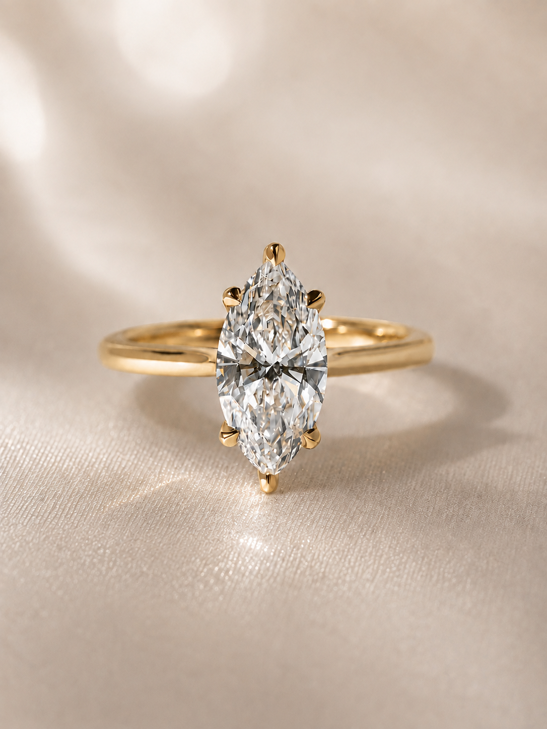 Close-up of a gold ring with a large marquise-cut diamond set in a prong setting, placed on a satin fabric background.