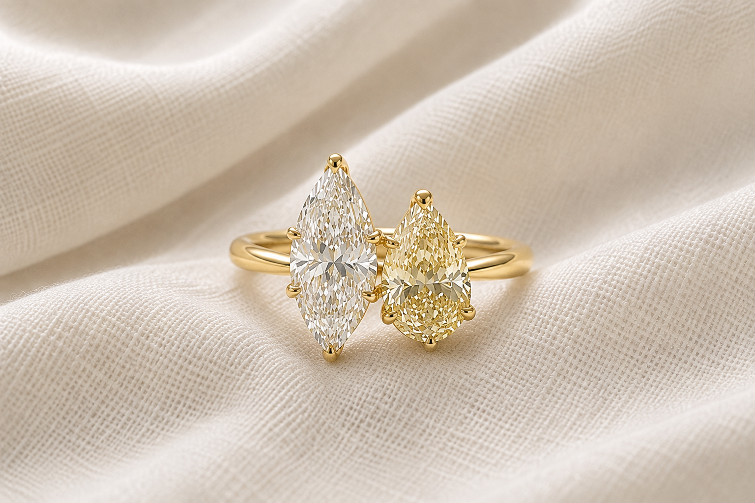 A toi et moi gold ring with two large marquise-cut diamond gemstones, one clear and one yellow, resting on beige fabric.