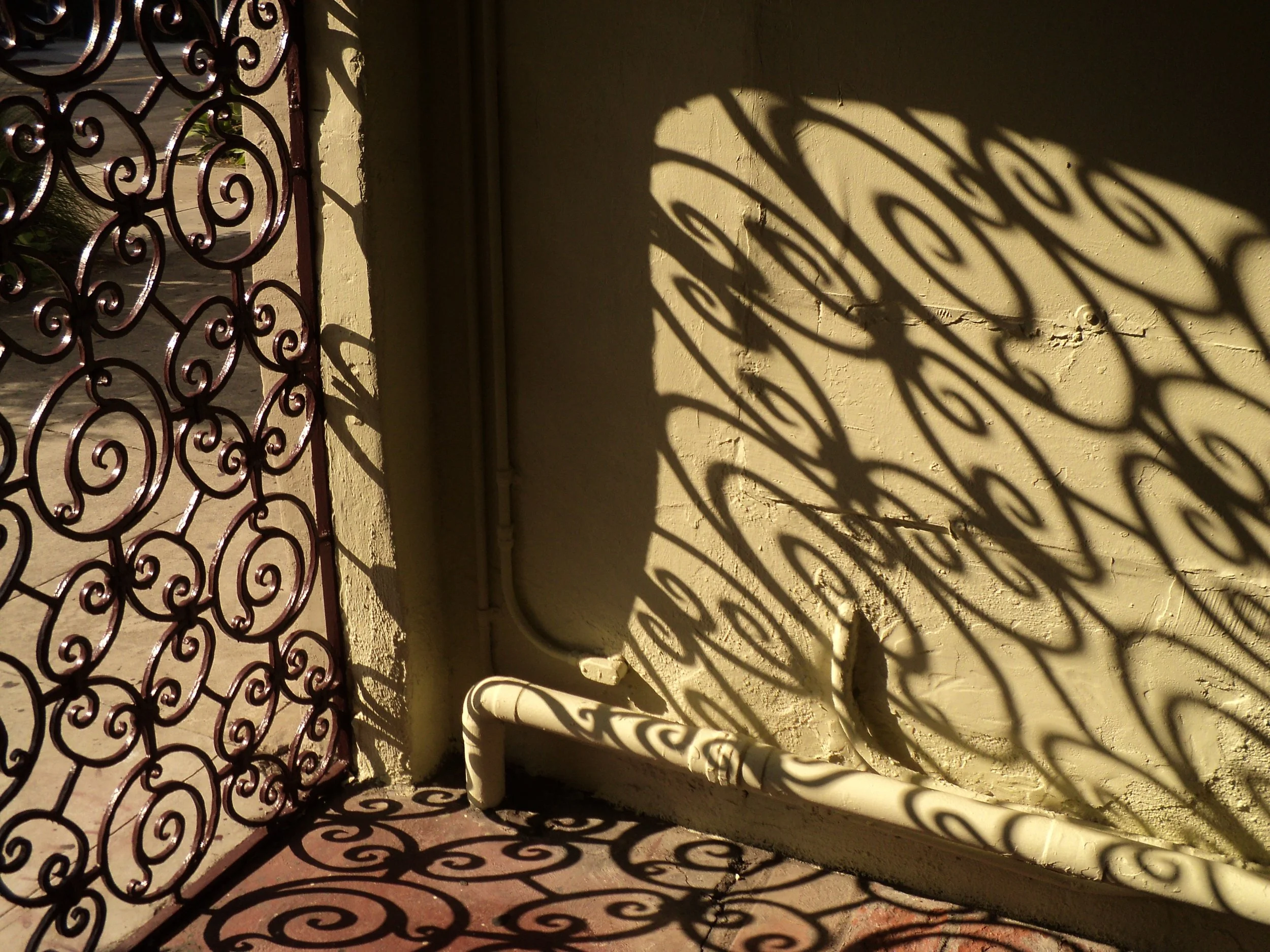 Shadow of a decorative wrought iron fence cast on a yellow wall.