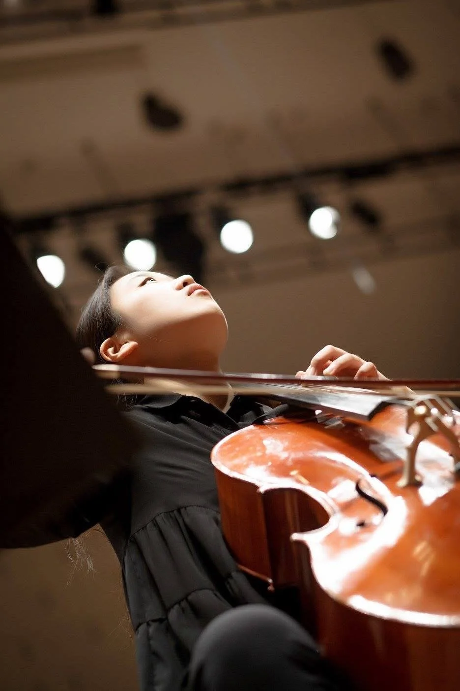 A young woman playing a violin on stage, viewed from below with stage lights overhead.