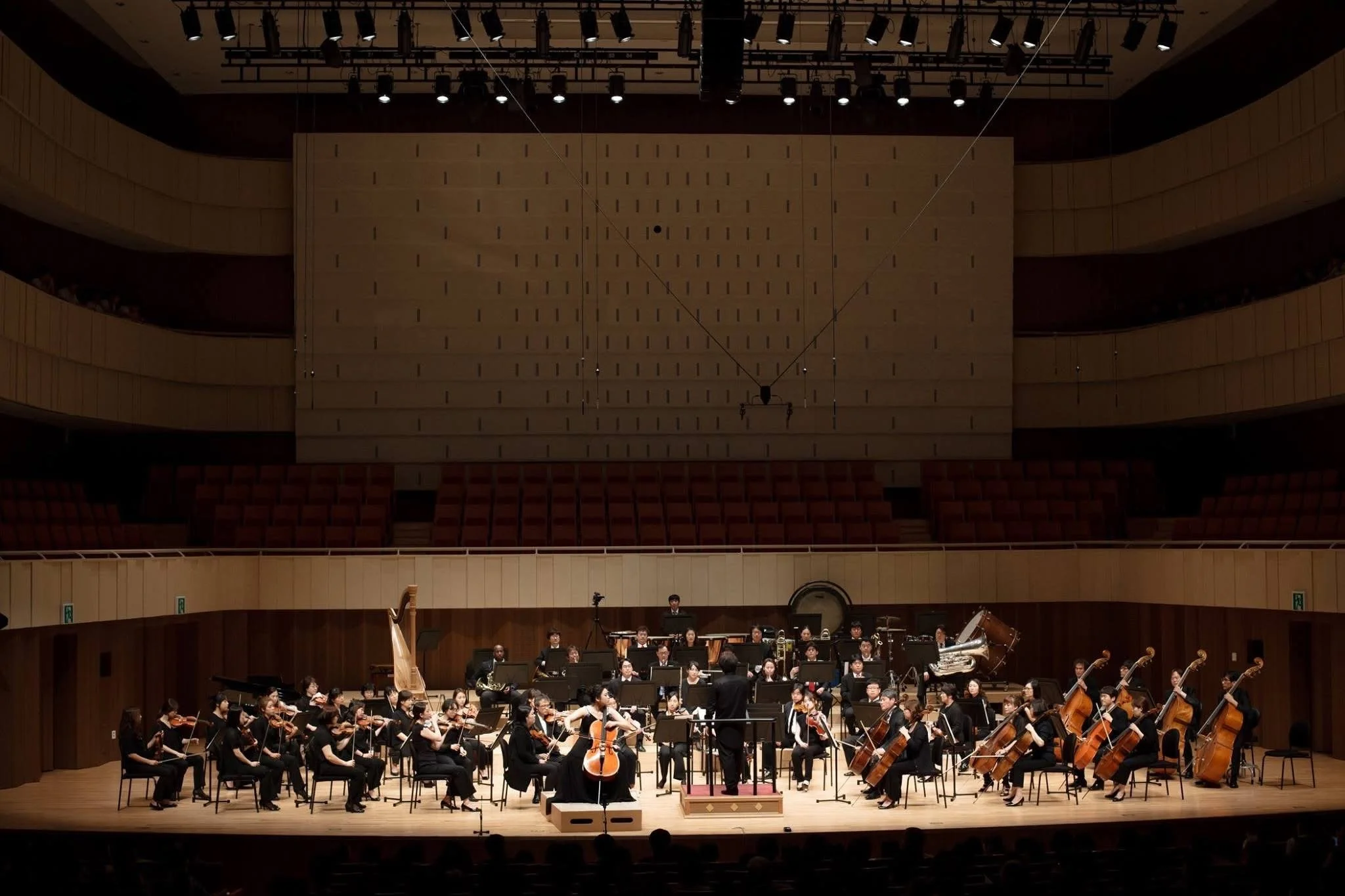 An orchestra performing on stage in a concert hall, with musicians playing various instruments.
