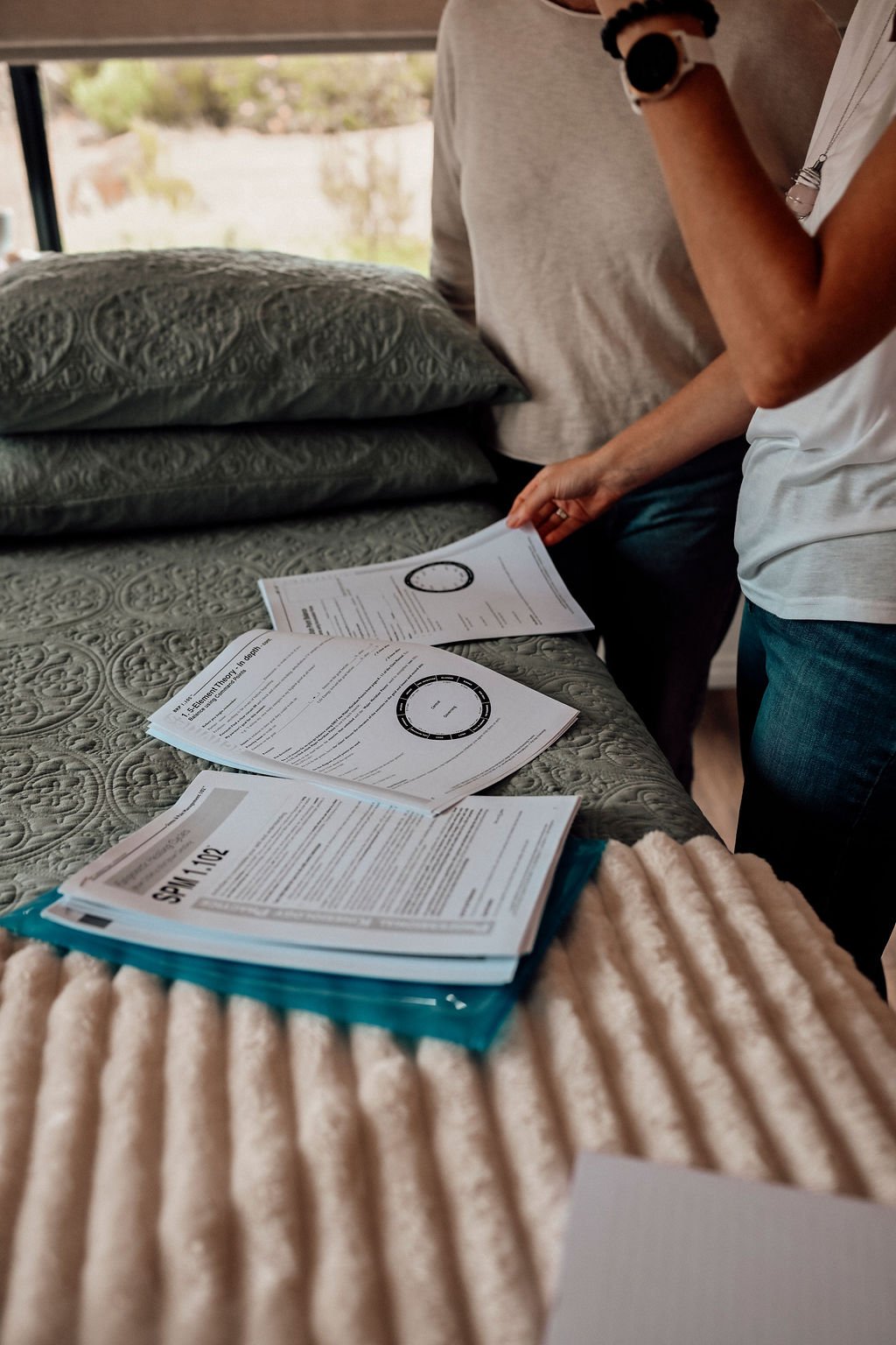 People looking at kinesiology charts or informational documents on a treatment table with pillows, with blurred background.