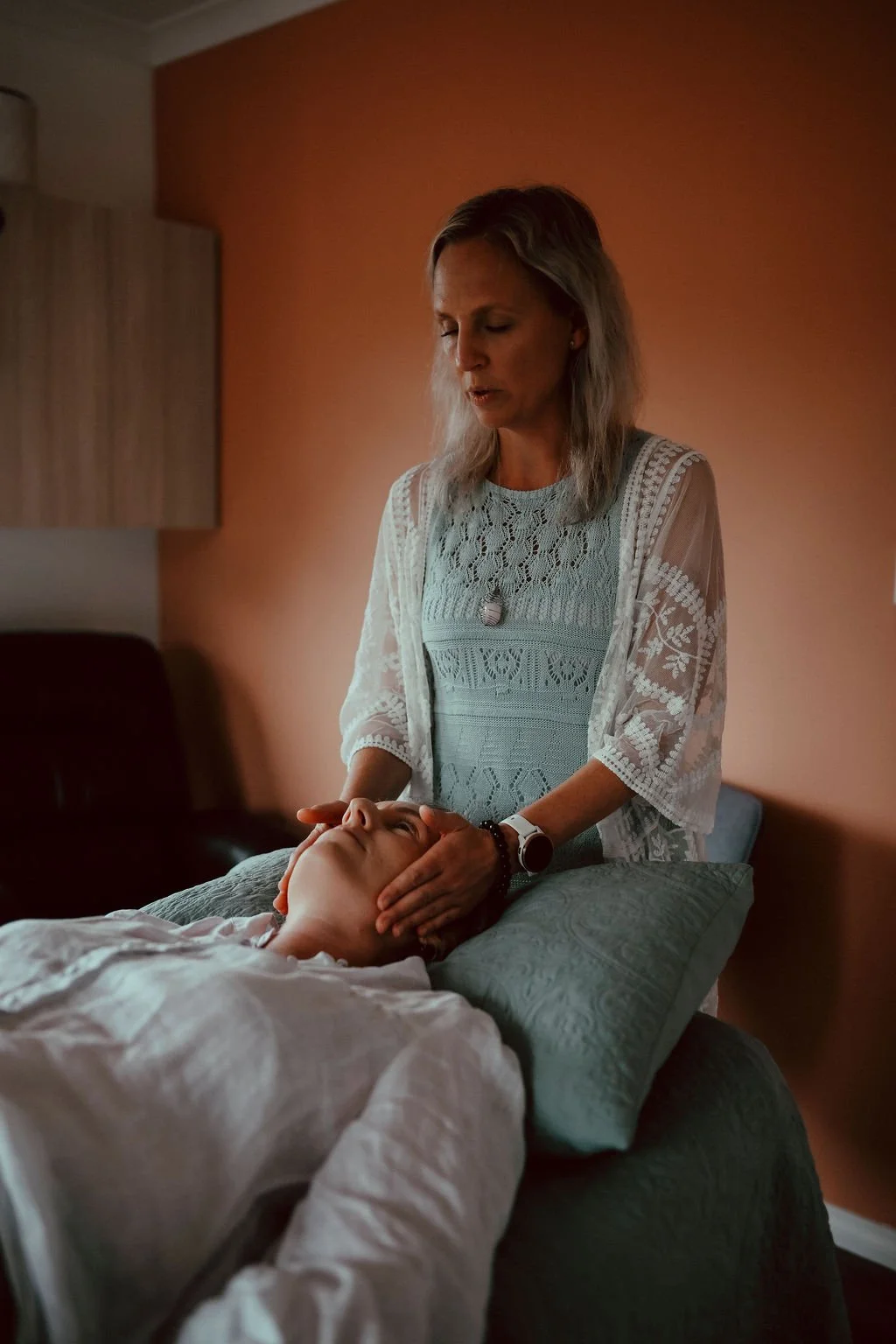Woman giving a kinesiology balance to a person lying on an examination table with a beige background.