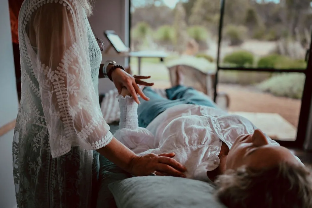 A person lying on a treatment table with eyes closed outdoors, receiving a kinesiology balance by  practitioner.