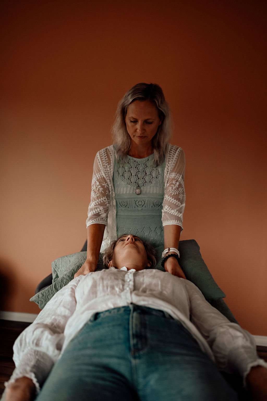 Woman giving a kinesiology balance to a person lying on an examination table with a beige background.