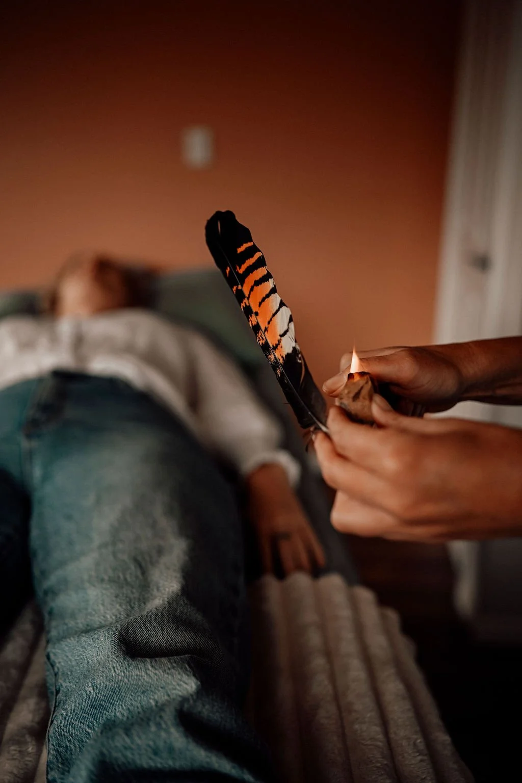 Close-up of a person holding a female red tail black cockatoo feather, while a woman is lying down in the background on a treatment table.
