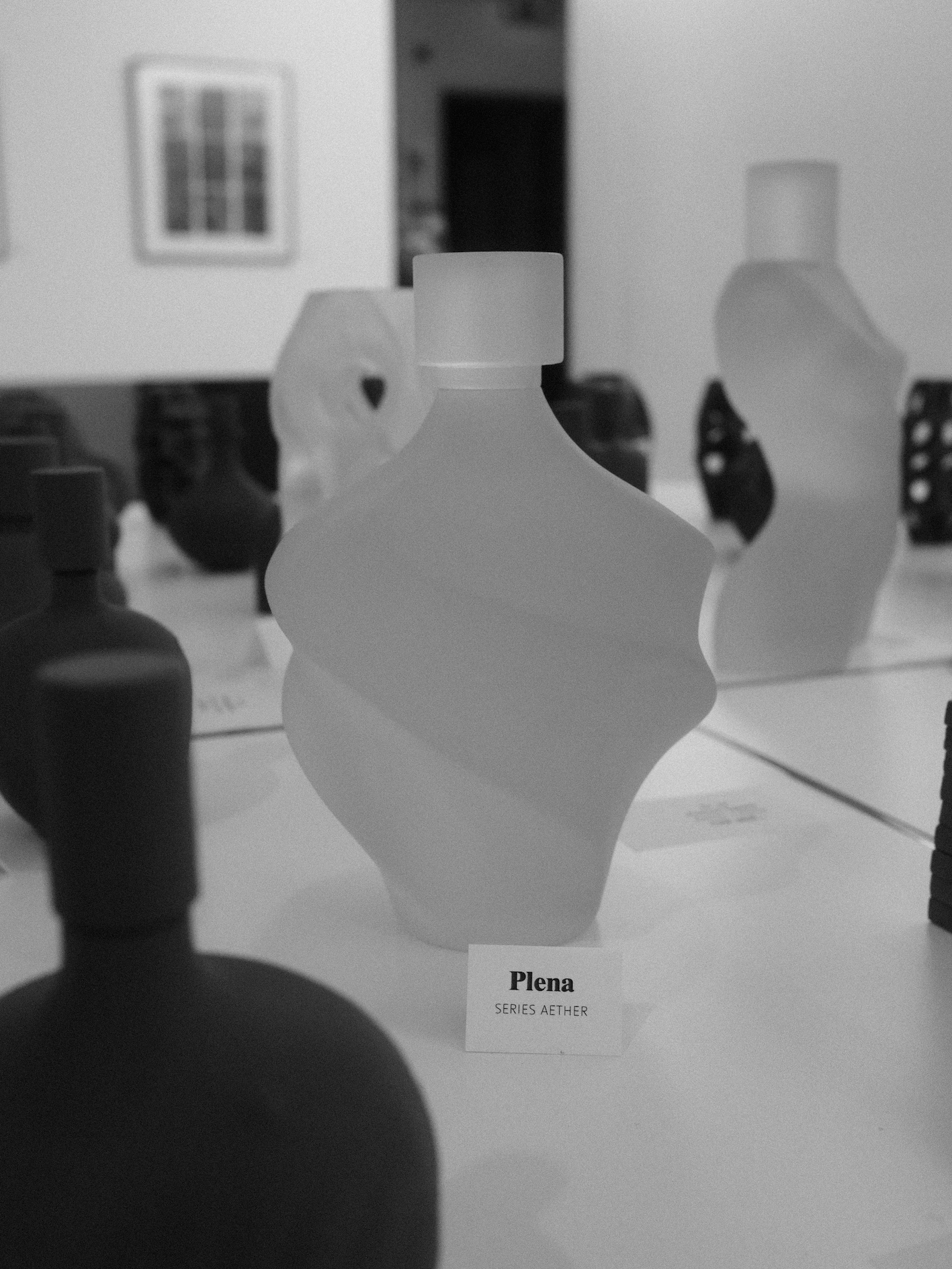 Black and white photo of a display with a porcelain vase labeled "Plena" in front and other vases in the background.
