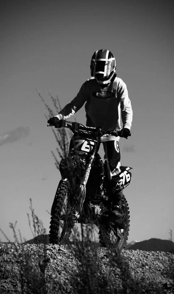 A person riding a motorcross bike on rough terrain wearing a full-face helmet and protective gear, black and white photo.