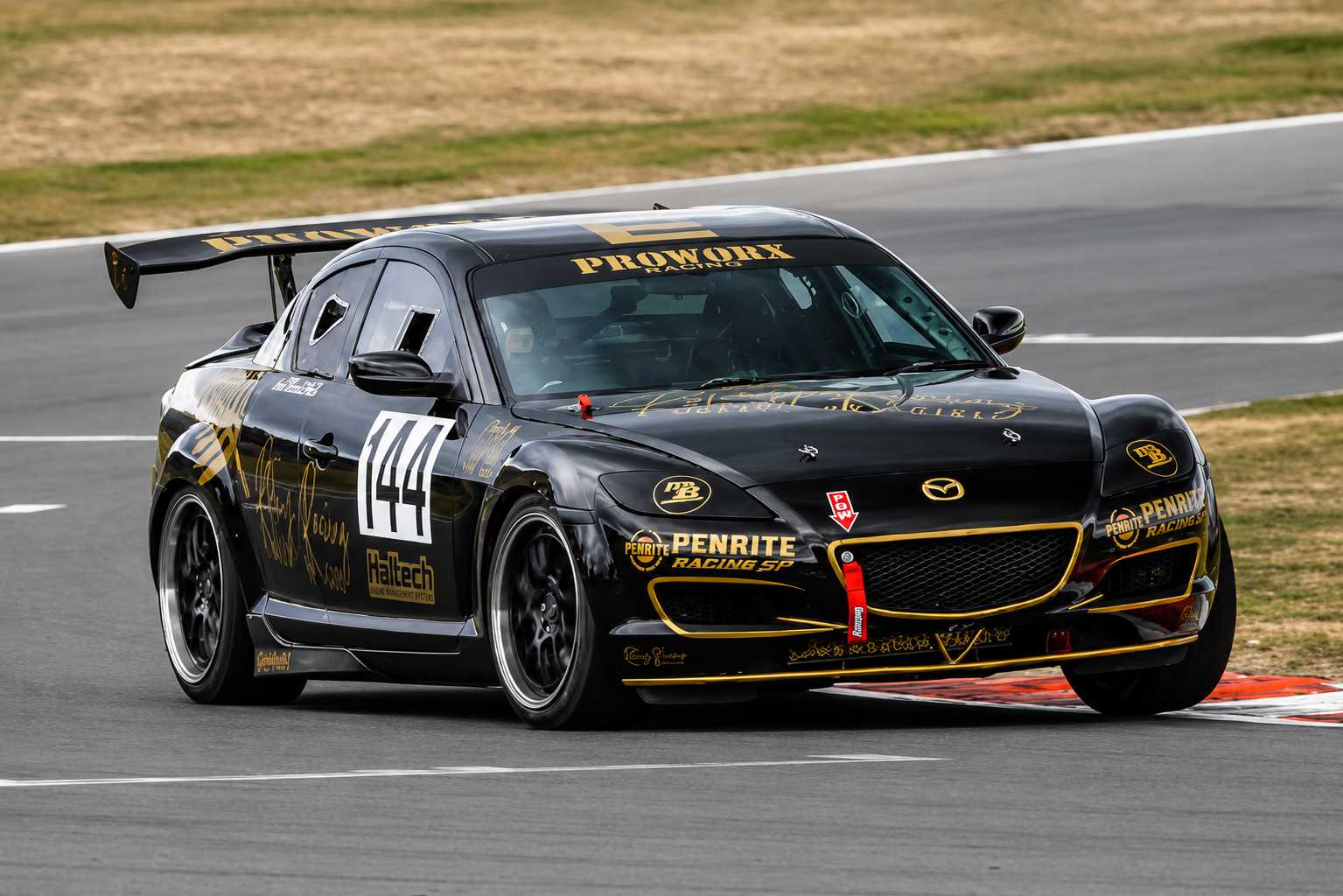 Black race car with yellow and gold decals and sponsorship logos, number 144, on a racetrack.