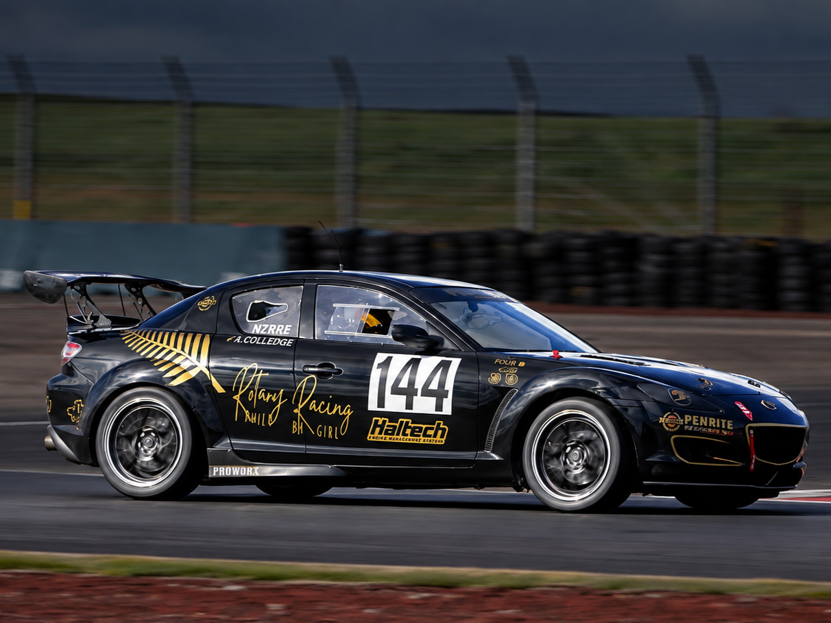 Race car on track with black and gold livery, number 144, racing branding, and a large rear spoiler.