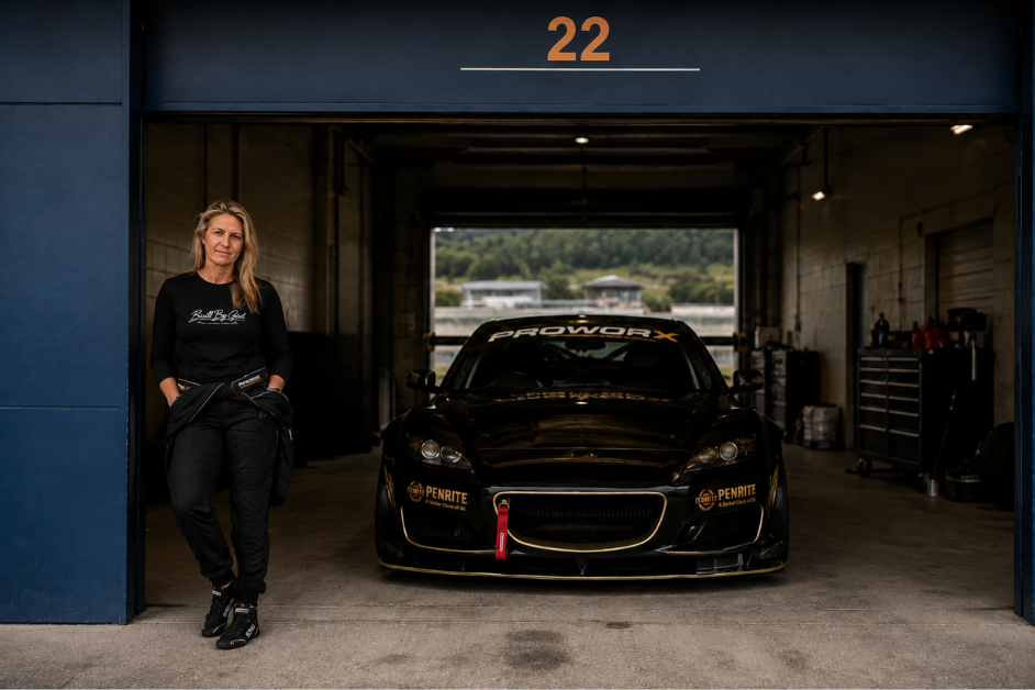 A woman standing next to a black race car inside a garage with the number 22 above the entrance.