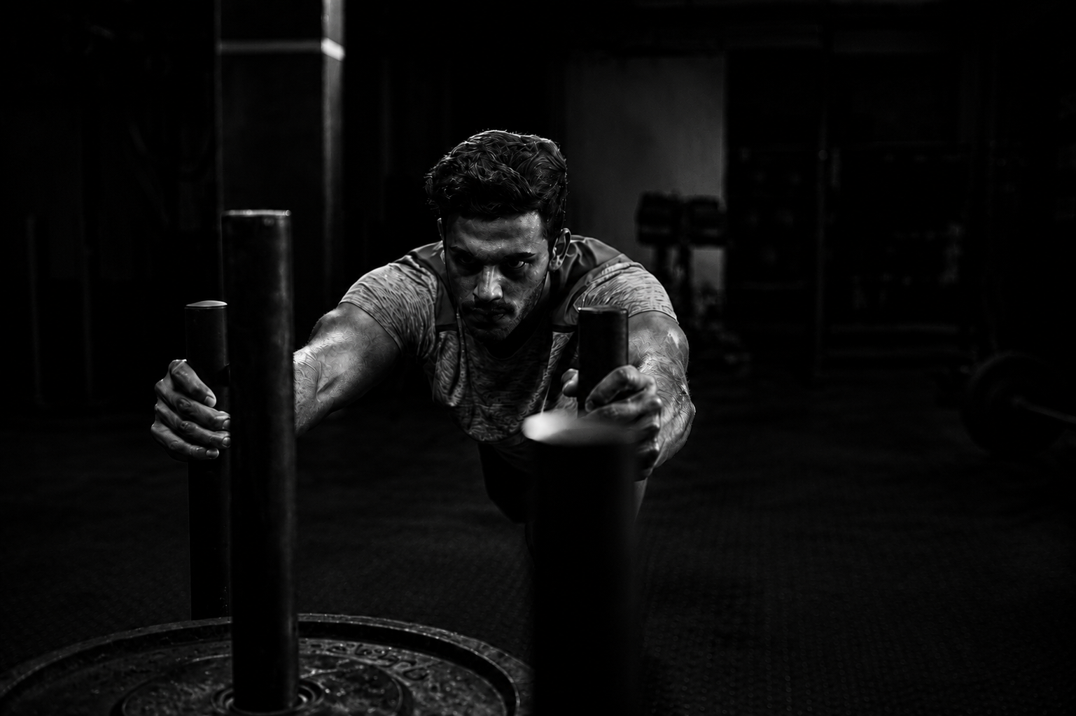 A man pushing a weighted sled in a gym with dim lighting.