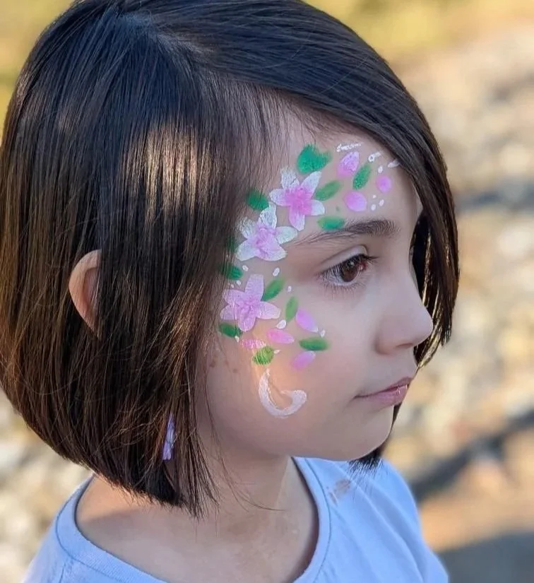Young girl with short brown hair and face paint of pink flowers, green leaves, and white accents on her right cheek and temple.