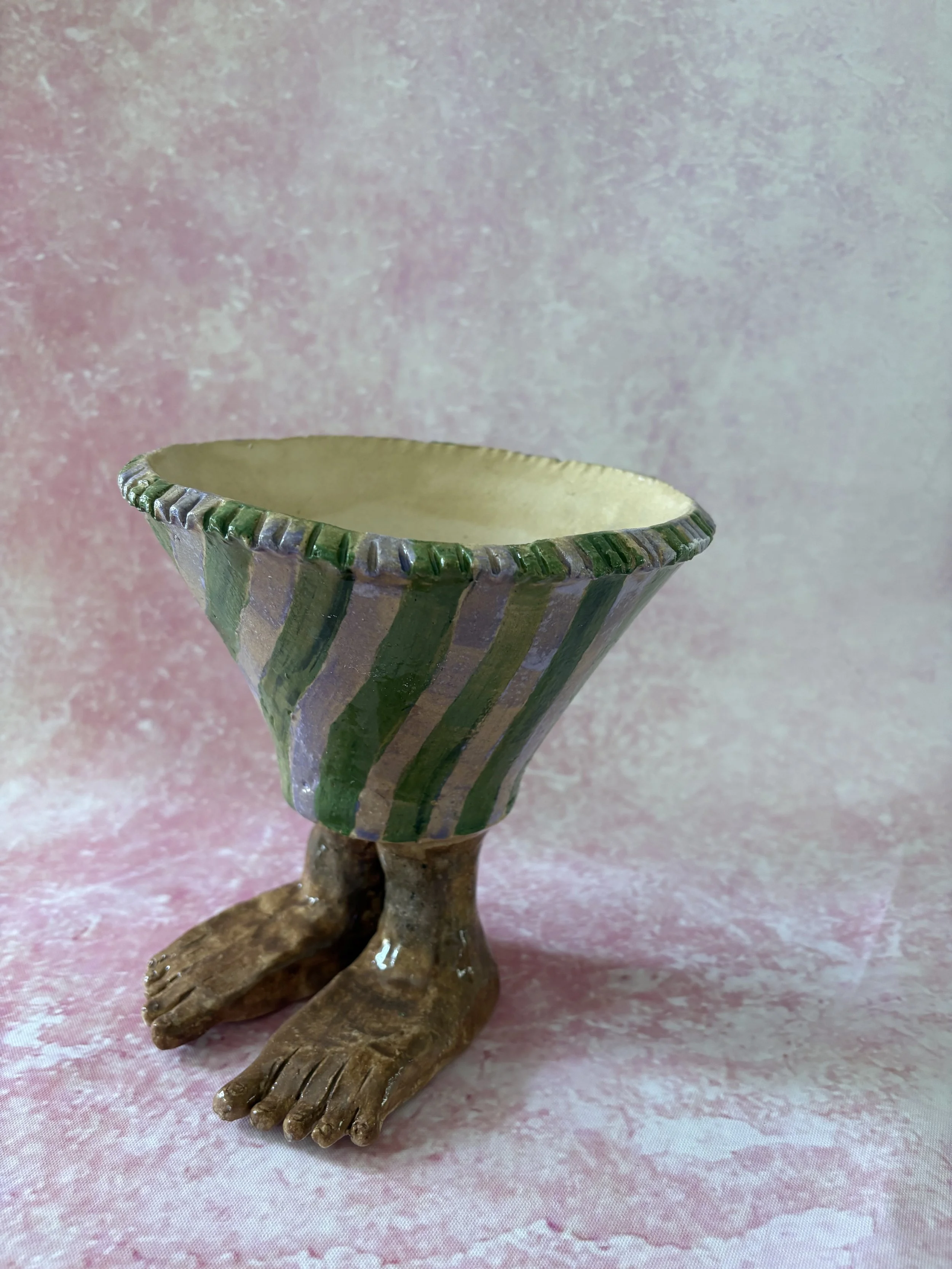 Plant pot with human feet, decorated with purple and green stripes.