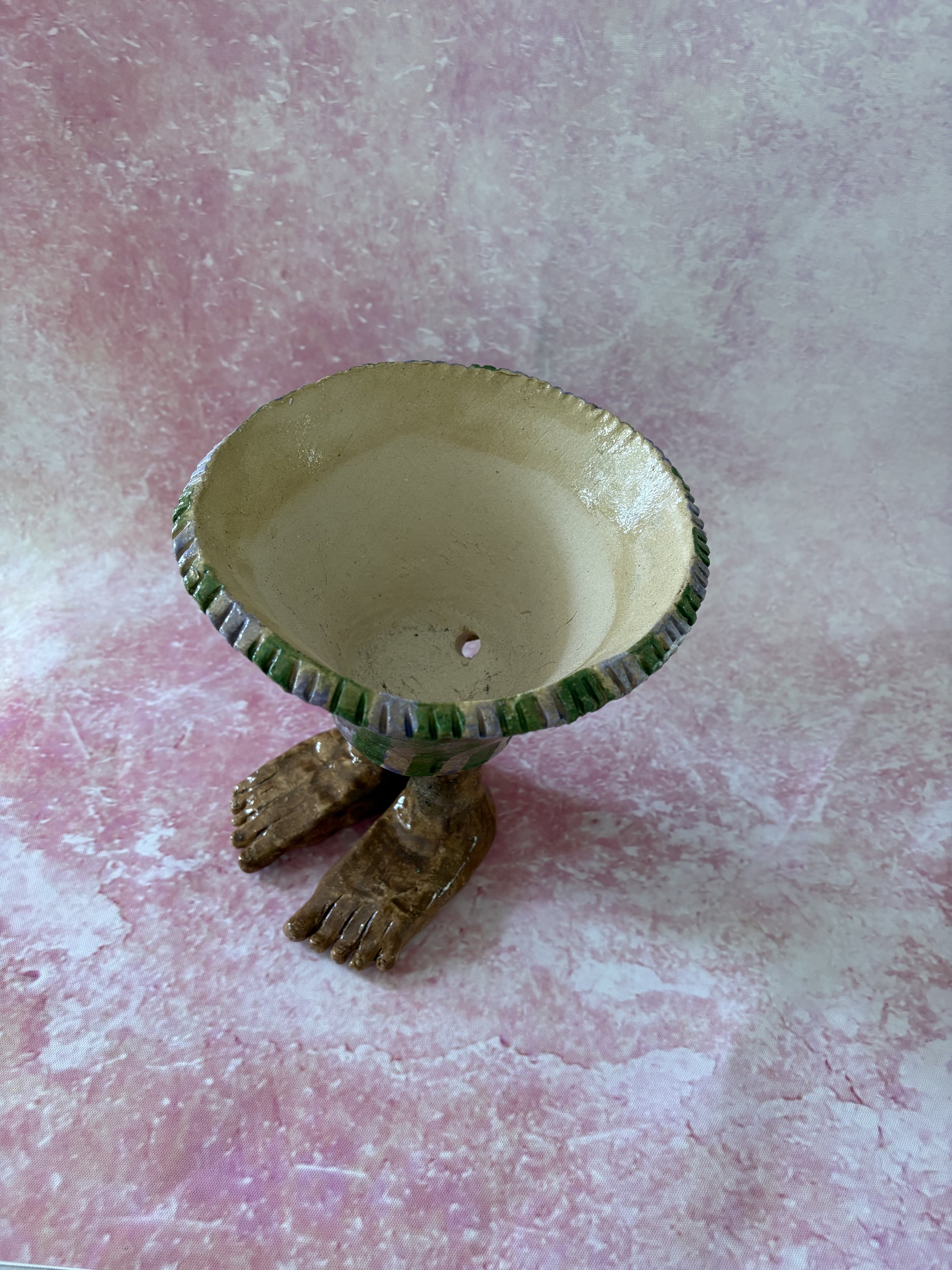 Plant pot with human feet, decorated with purple and green stripes.